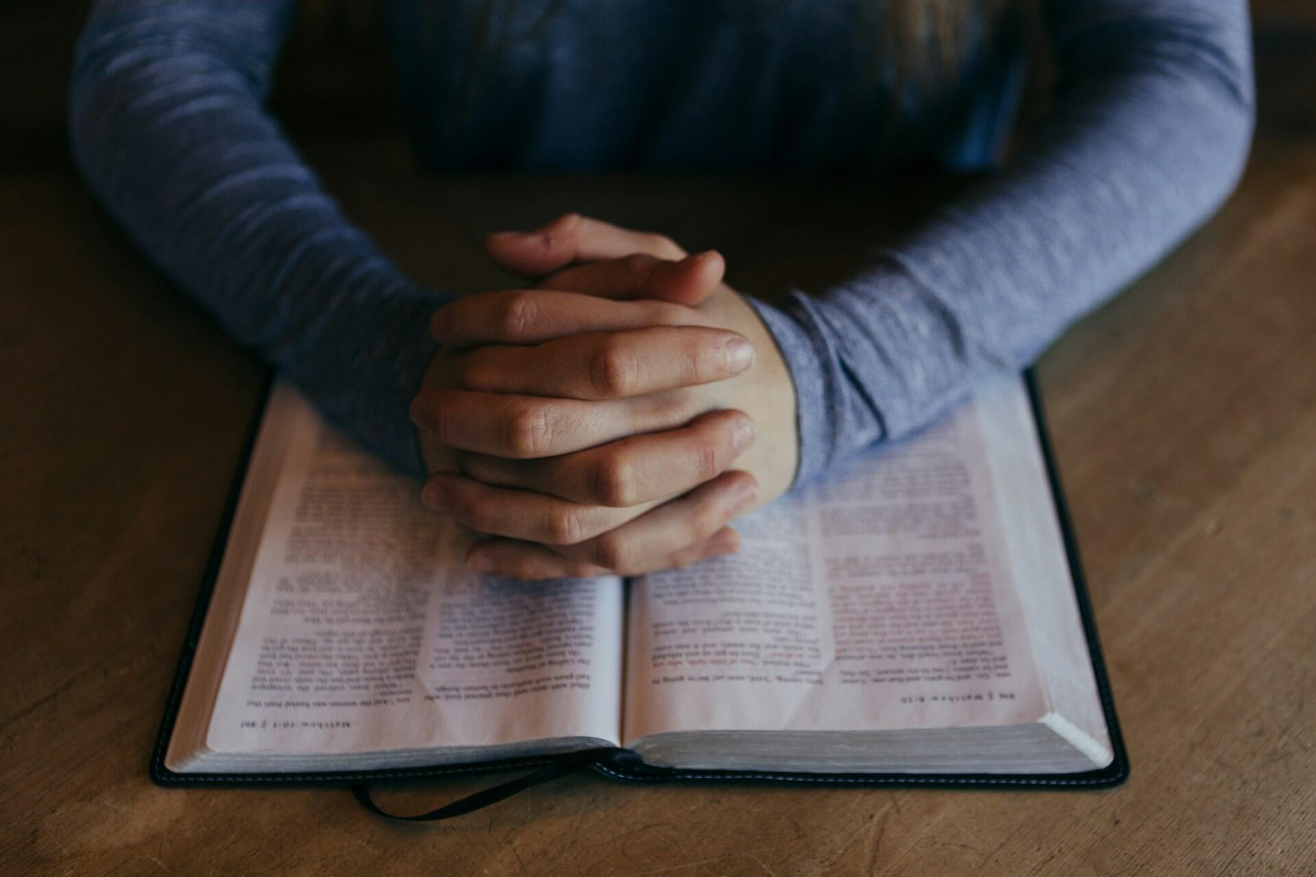 Clasped hands resting on an open Bible