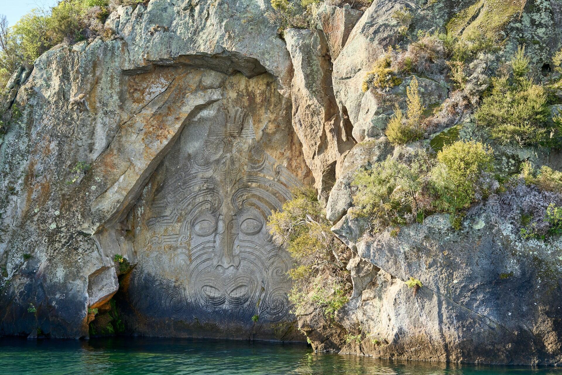 Large carved face in a rock wall beside green water
