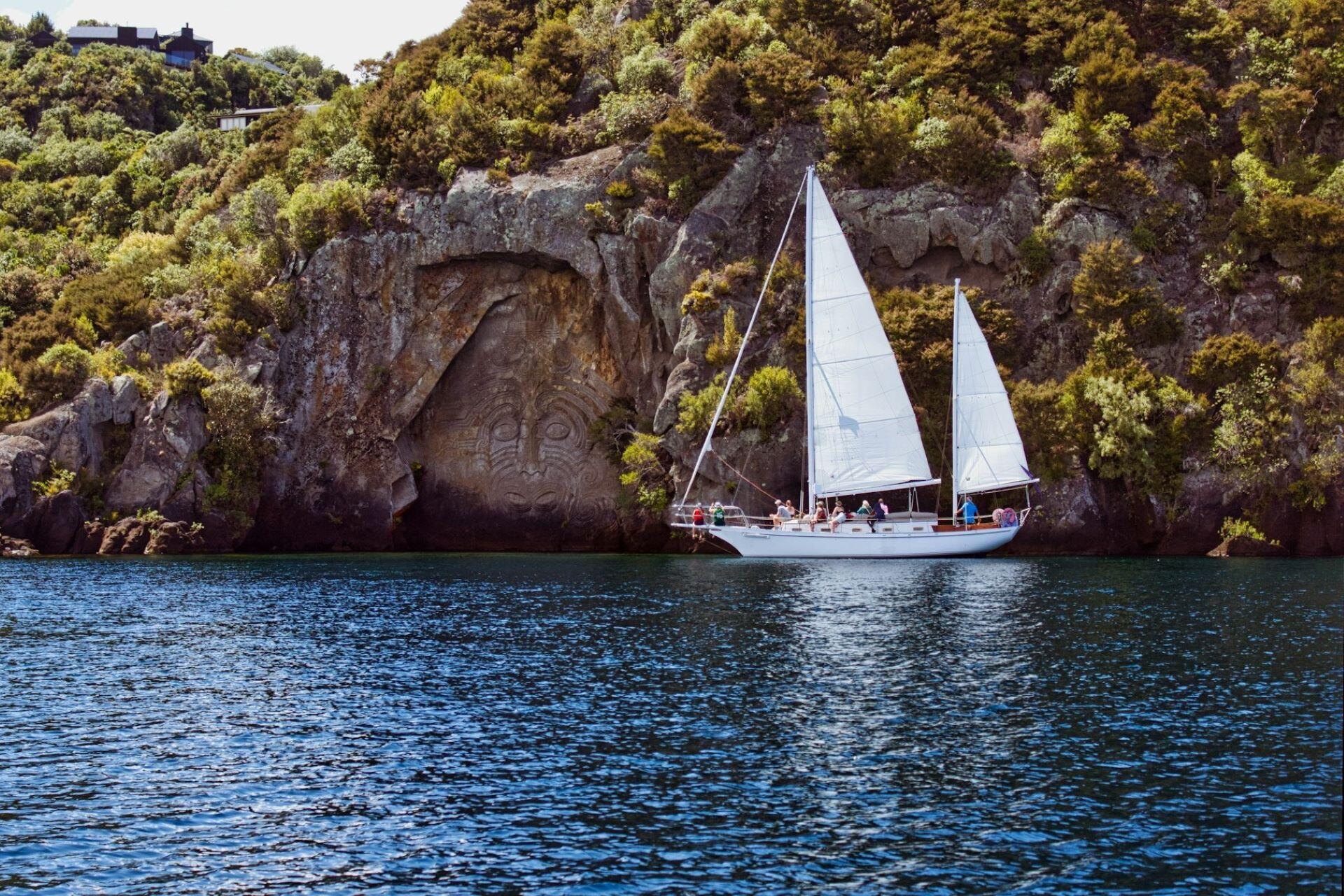 Sailboat on a lake beside a large Māori rock carving