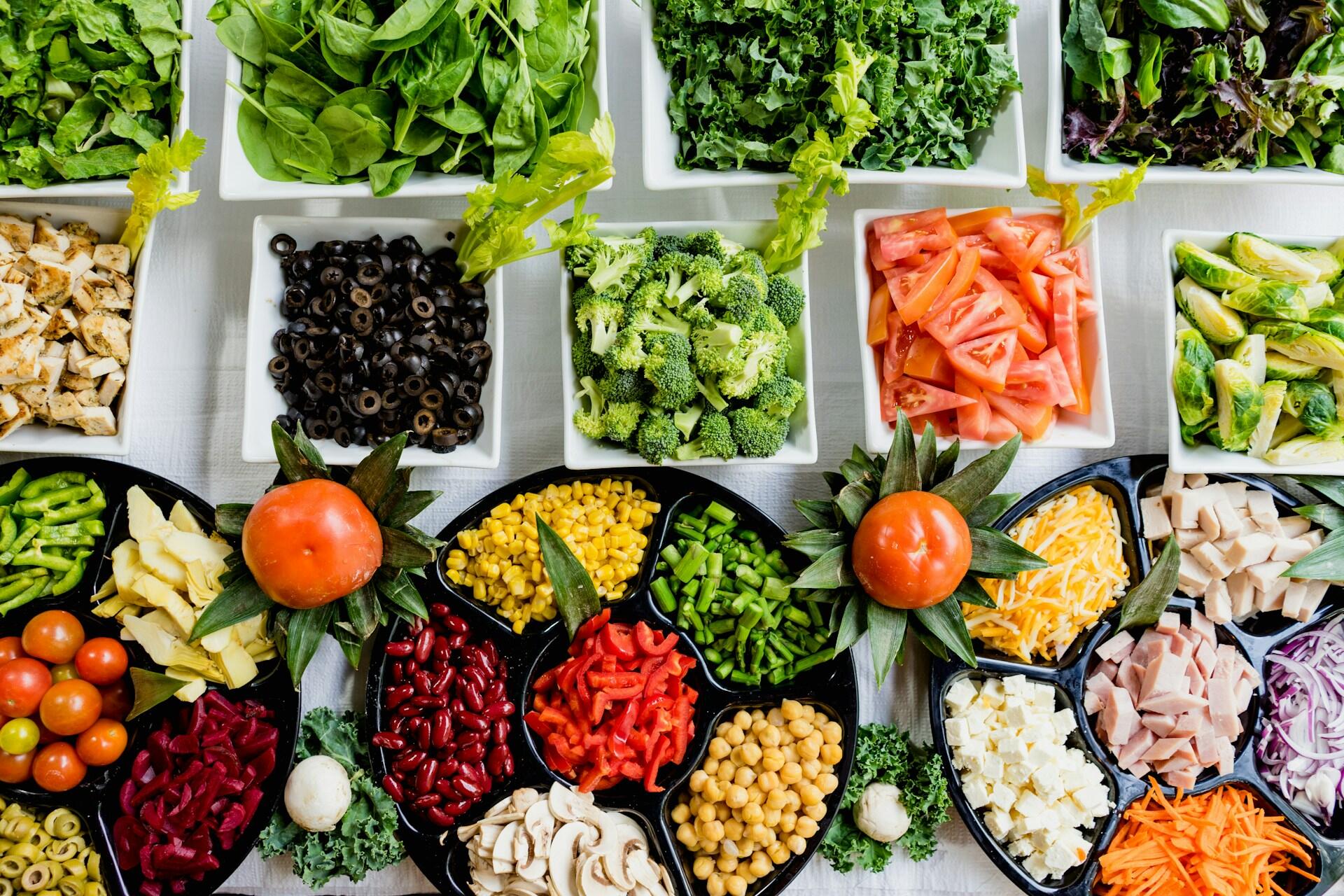 Bowls and trays filled with salad vegetables, beans, olives, cheese and sliced meat