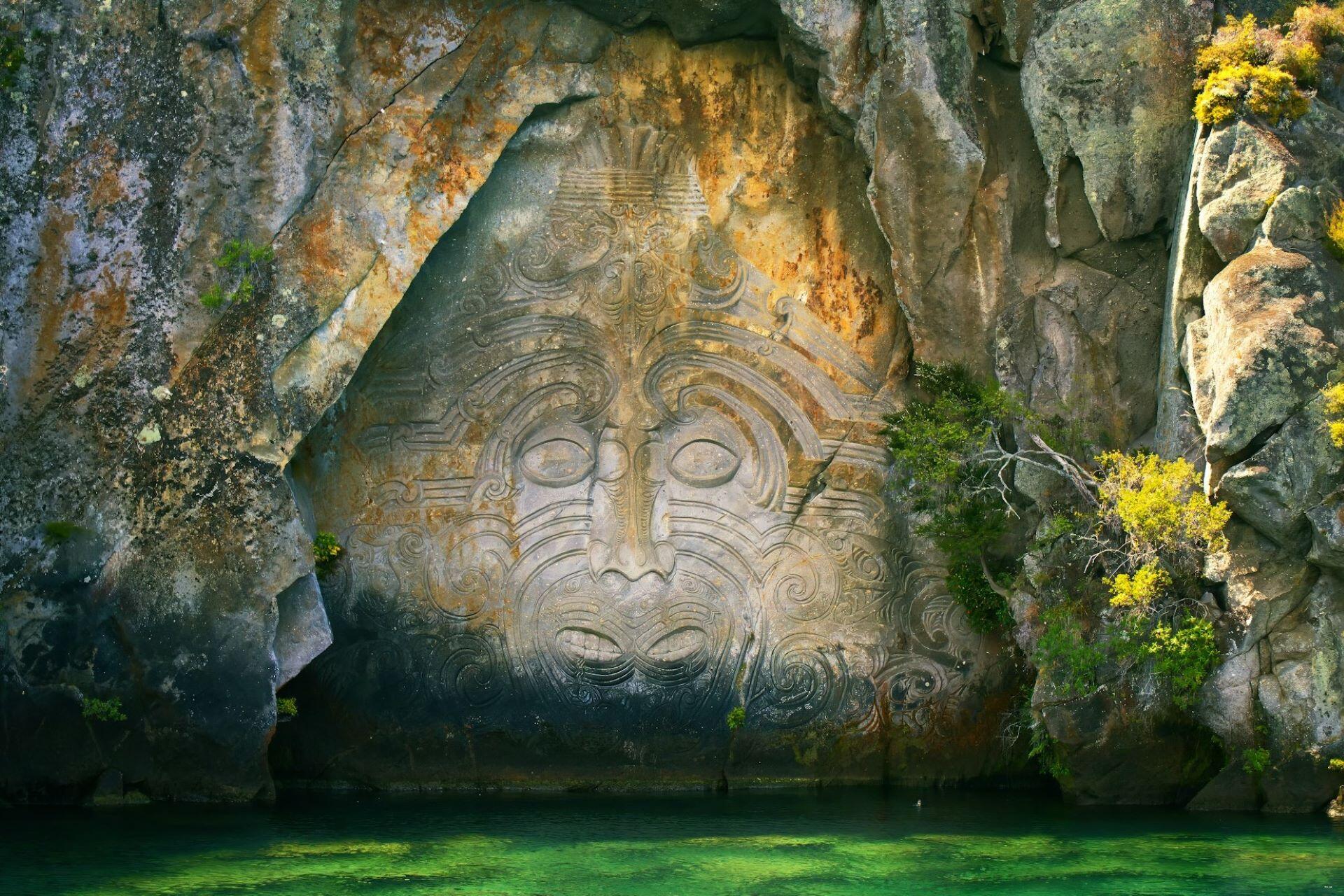Large carved face in a rock wall above green water
