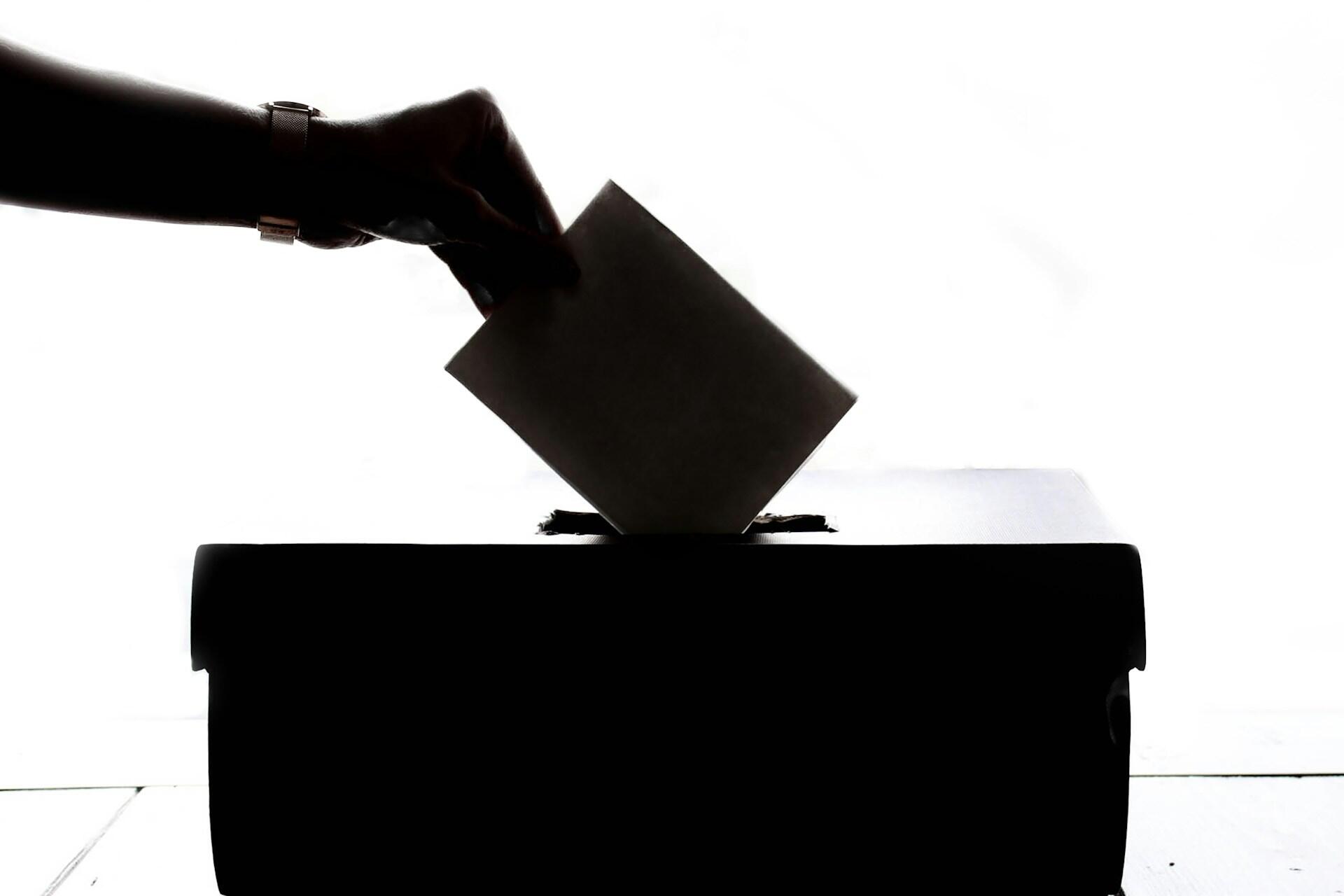 Silhouetted hand placing a ballot paper into a ballot box