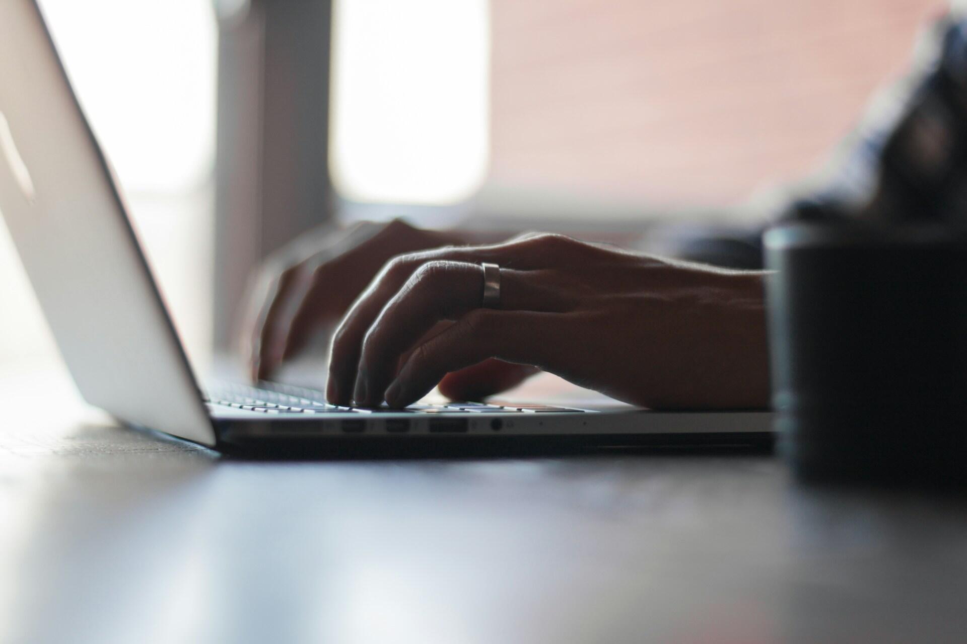 Hands typing on a laptop keyboard beside a dark mug