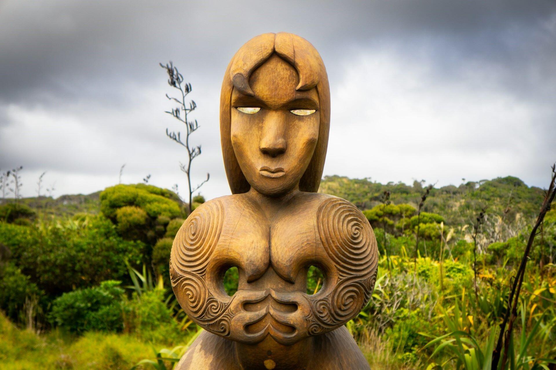Wooden Māori figure carving surrounded by native green vegetation