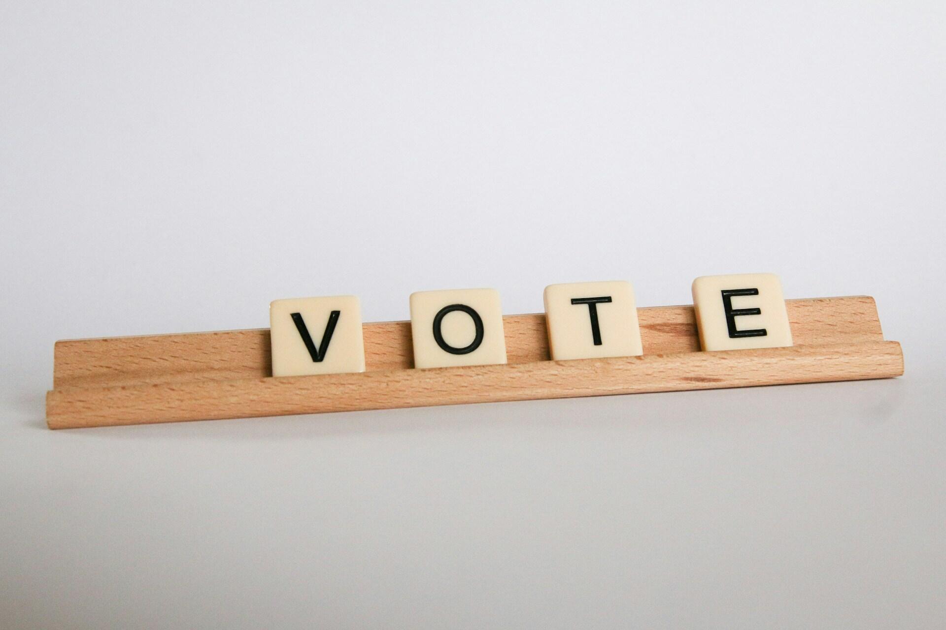 Letter tiles spelling VOTE arranged on a wooden rack