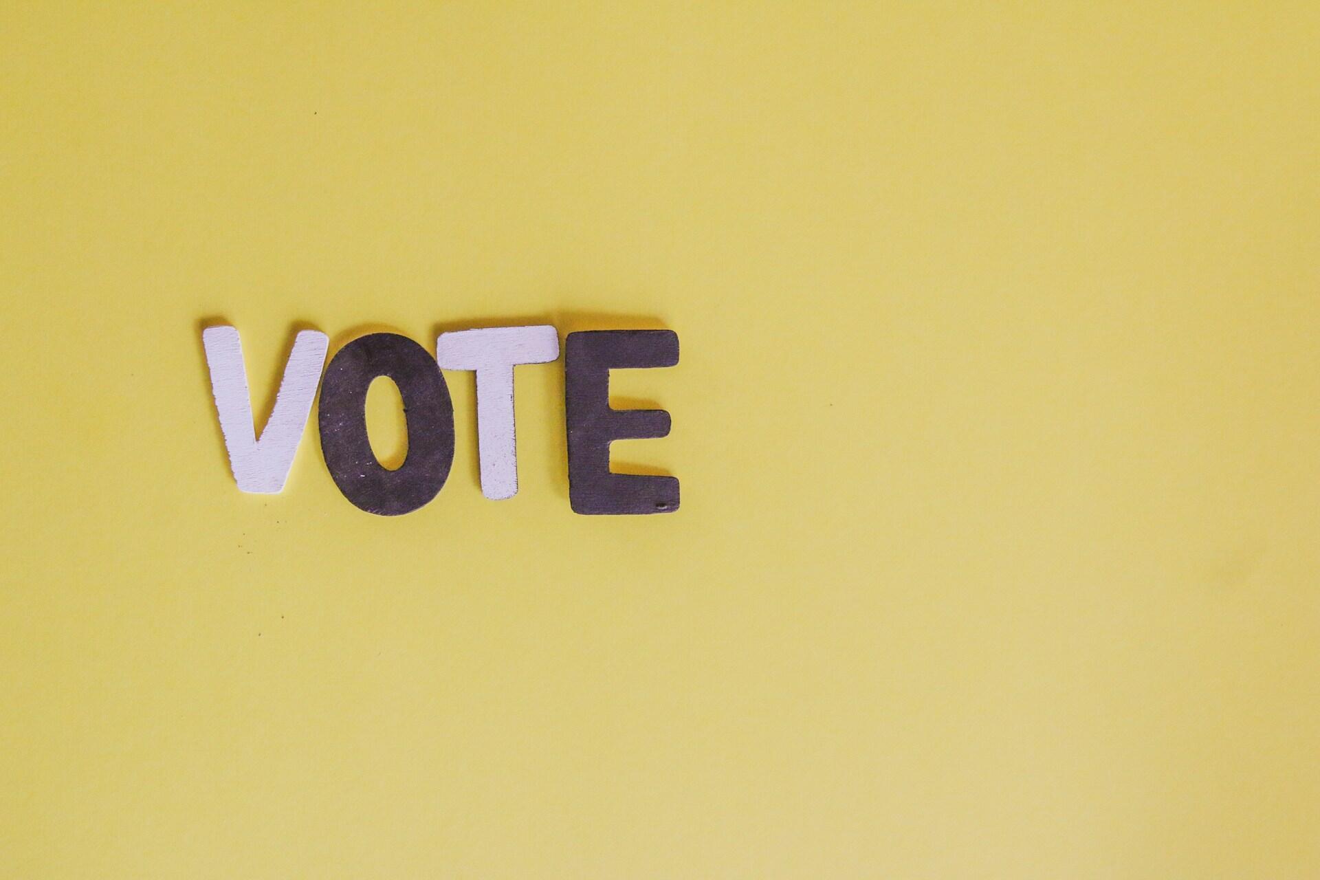 Wooden letters spelling VOTE on a yellow background