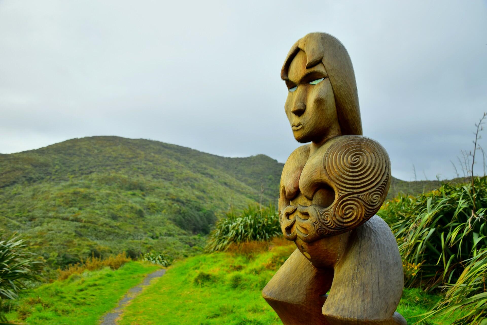 Carved wooden figure beside a path through green hills