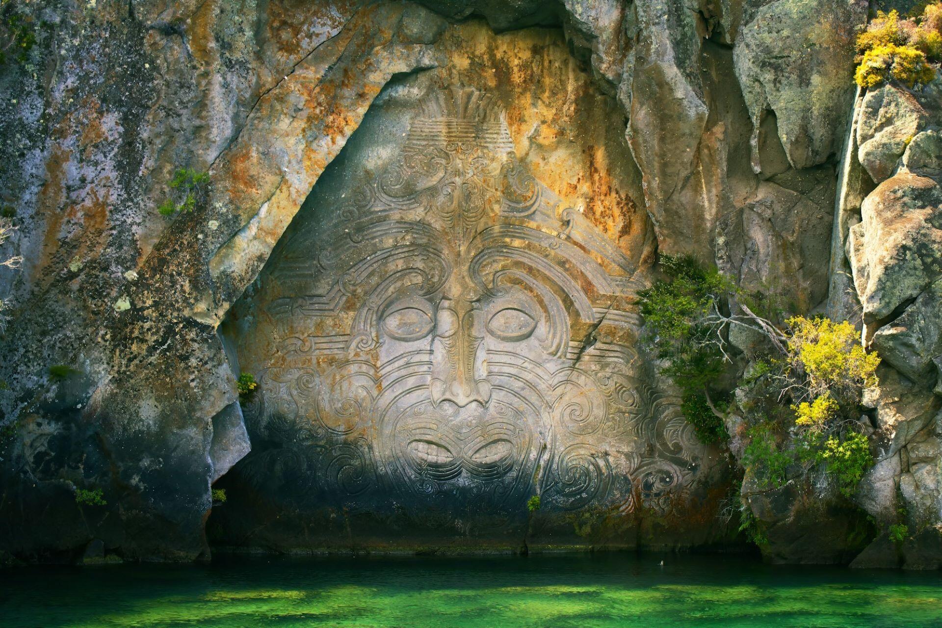 Large Māori rock carving beside the water in New Zealand