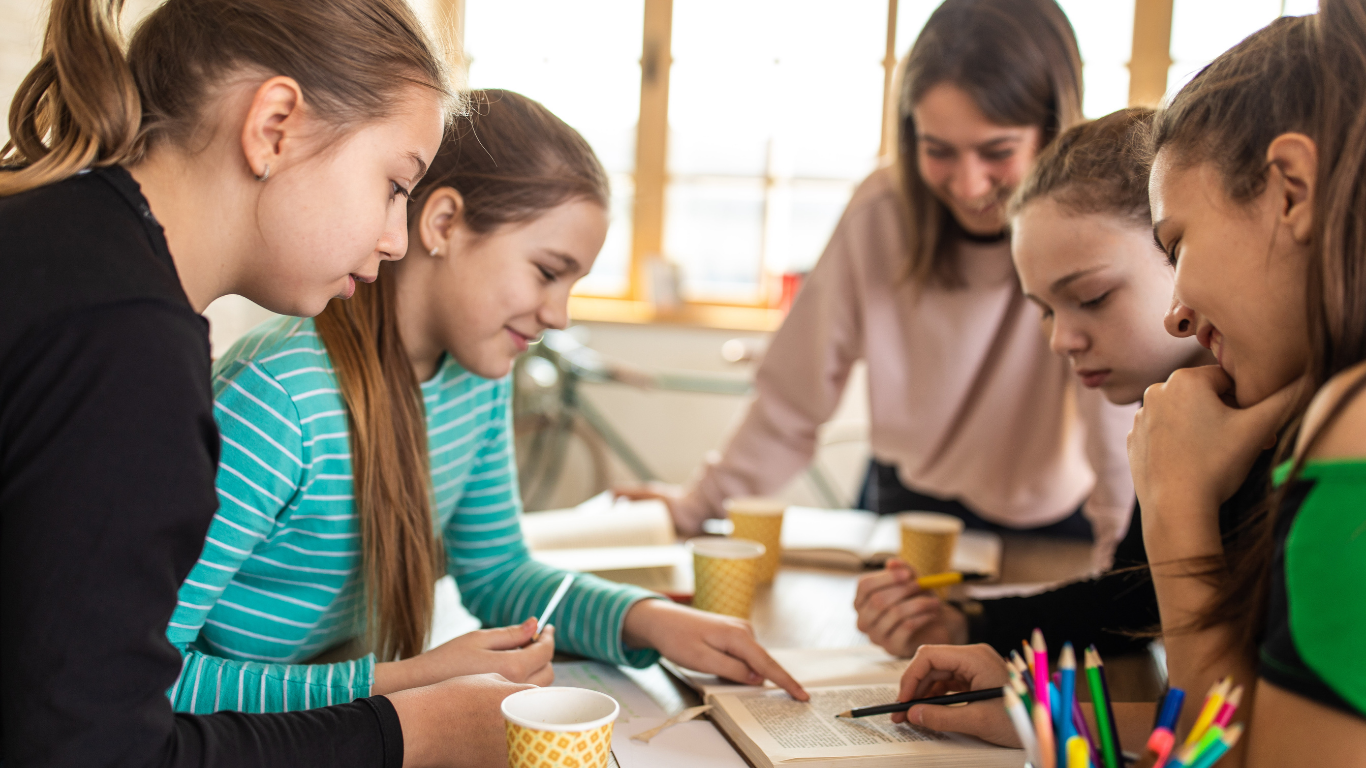 Grupo de jóvenes estudiantes trabajando juntas en un proyecto, rodeadas de libros y material escolar en un ambiente colaborativo.