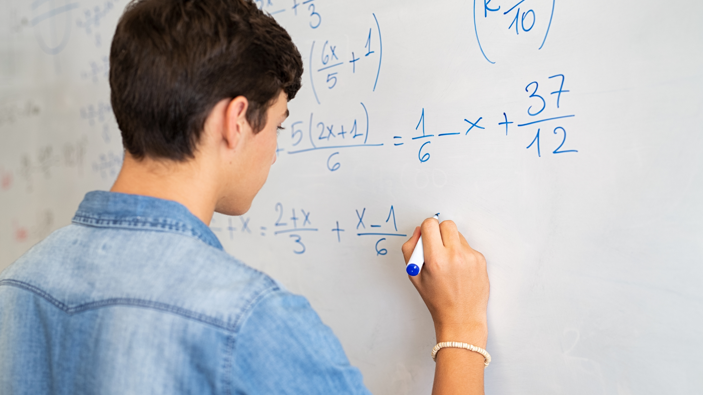 Estudiante resolviendo ecuaciones matemáticas en una pizarra blanca con marcador azul.