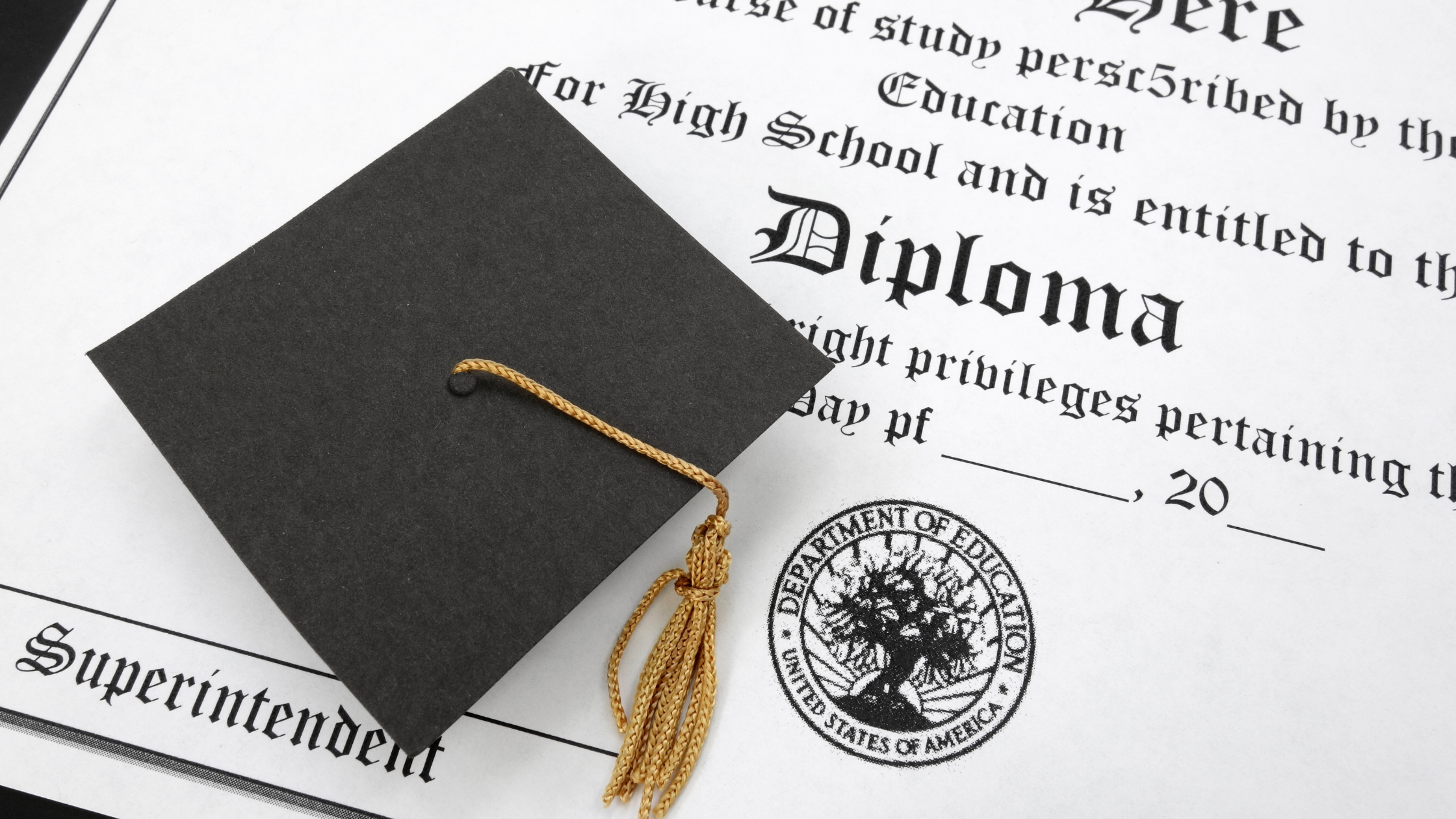 Birrete negro con borla dorada sobre un diploma impreso en inglés, destacando un sello oficial del Departamento de Educación.