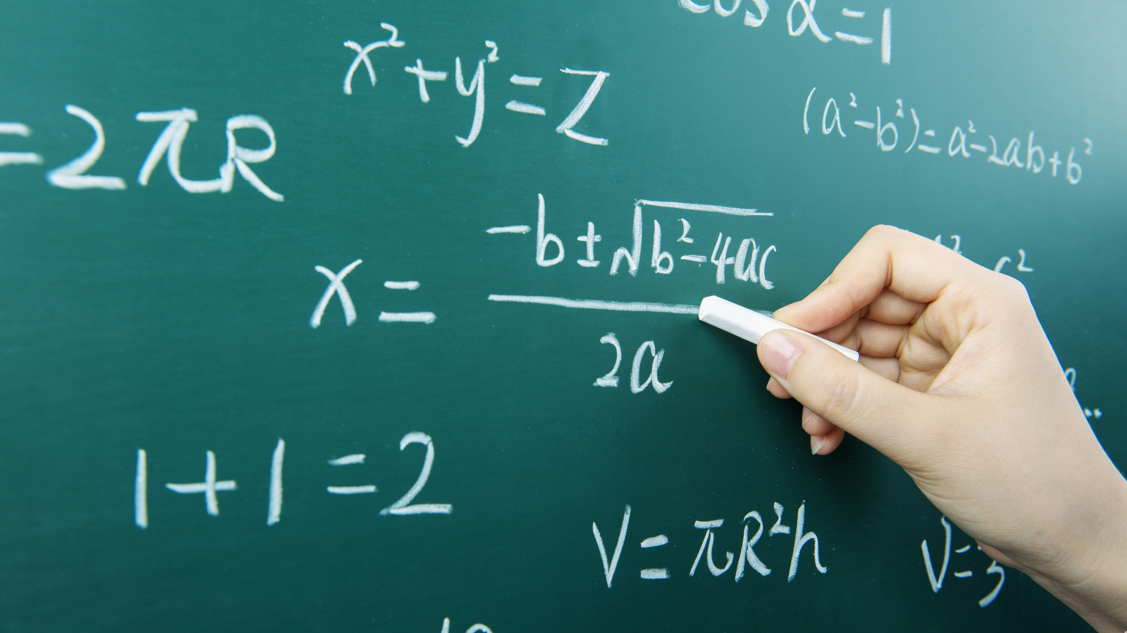 Mano escribiendo ecuaciones matemáticas en una pizarra verde con tiza blanca, incluyendo fórmulas algebraicas y operaciones.
