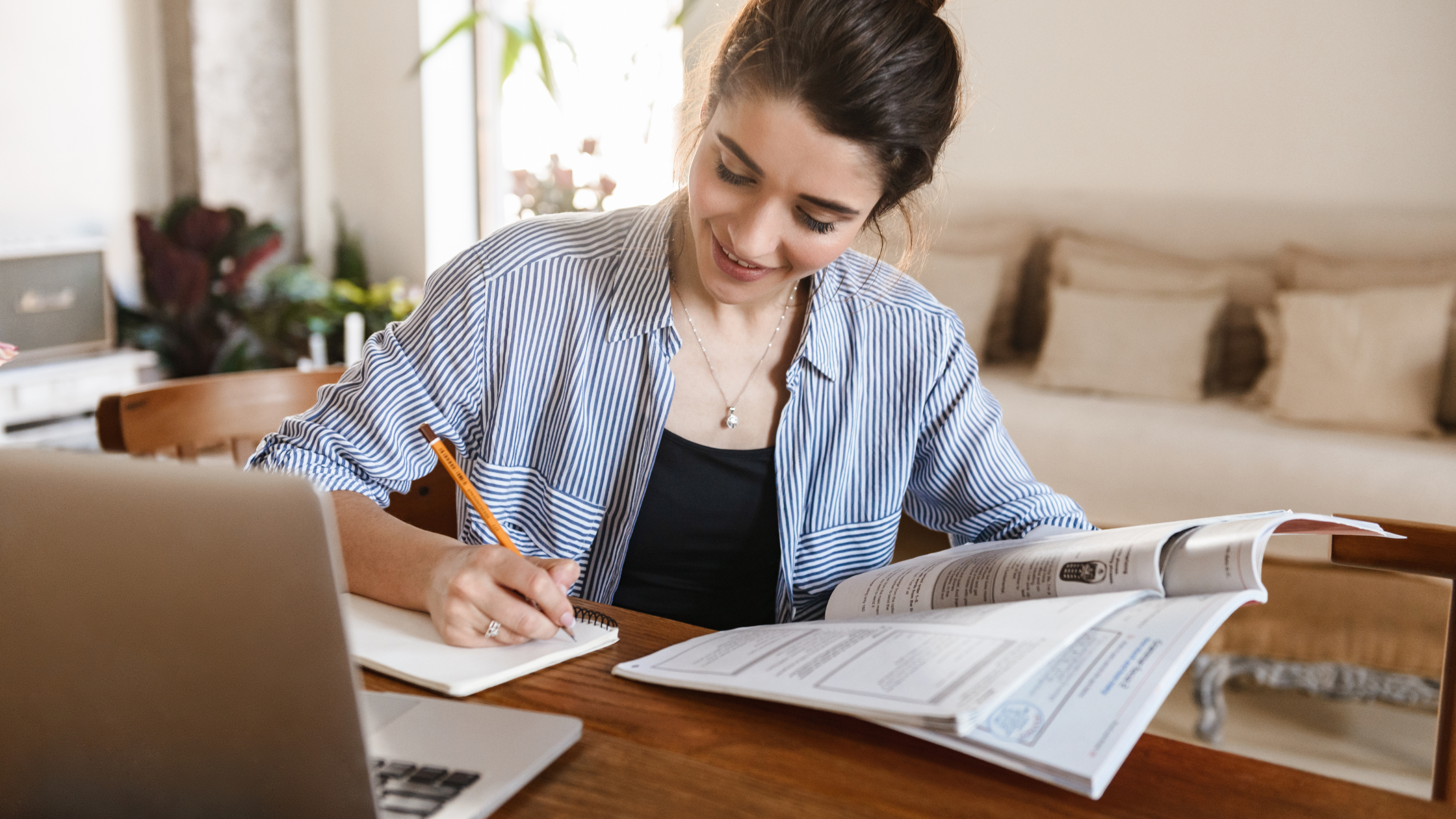 Mujer estudiando en casa con computadora y libros.