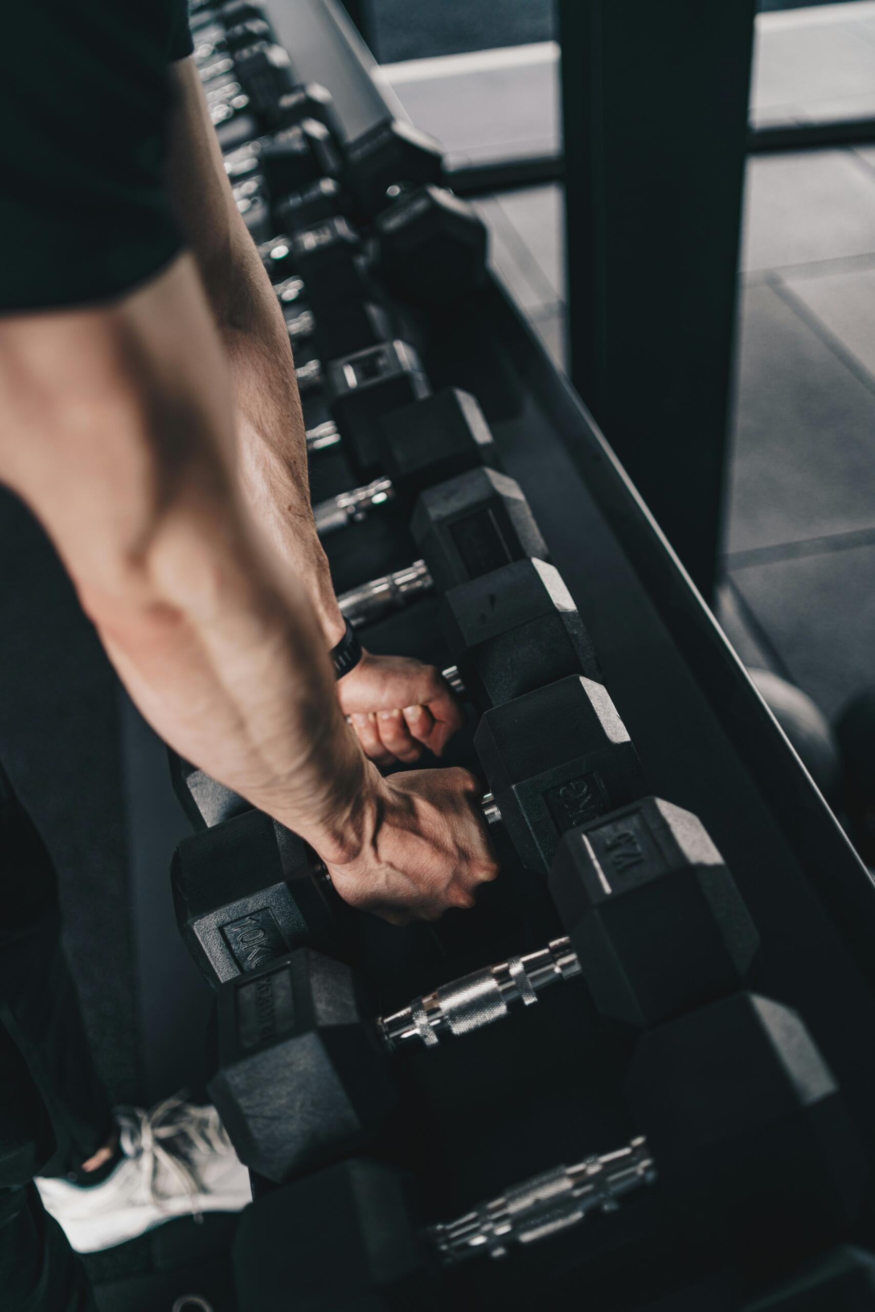 Hombre seleccionando mancuernas en un gimnasio para iniciar su rutina de pesas.