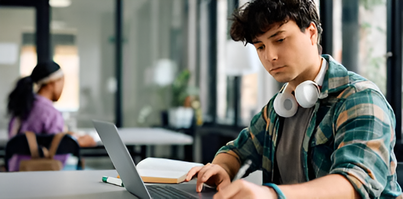 Un joven estudiante toma notas mientras aprende en línea en una computadora portátil en la universidad.