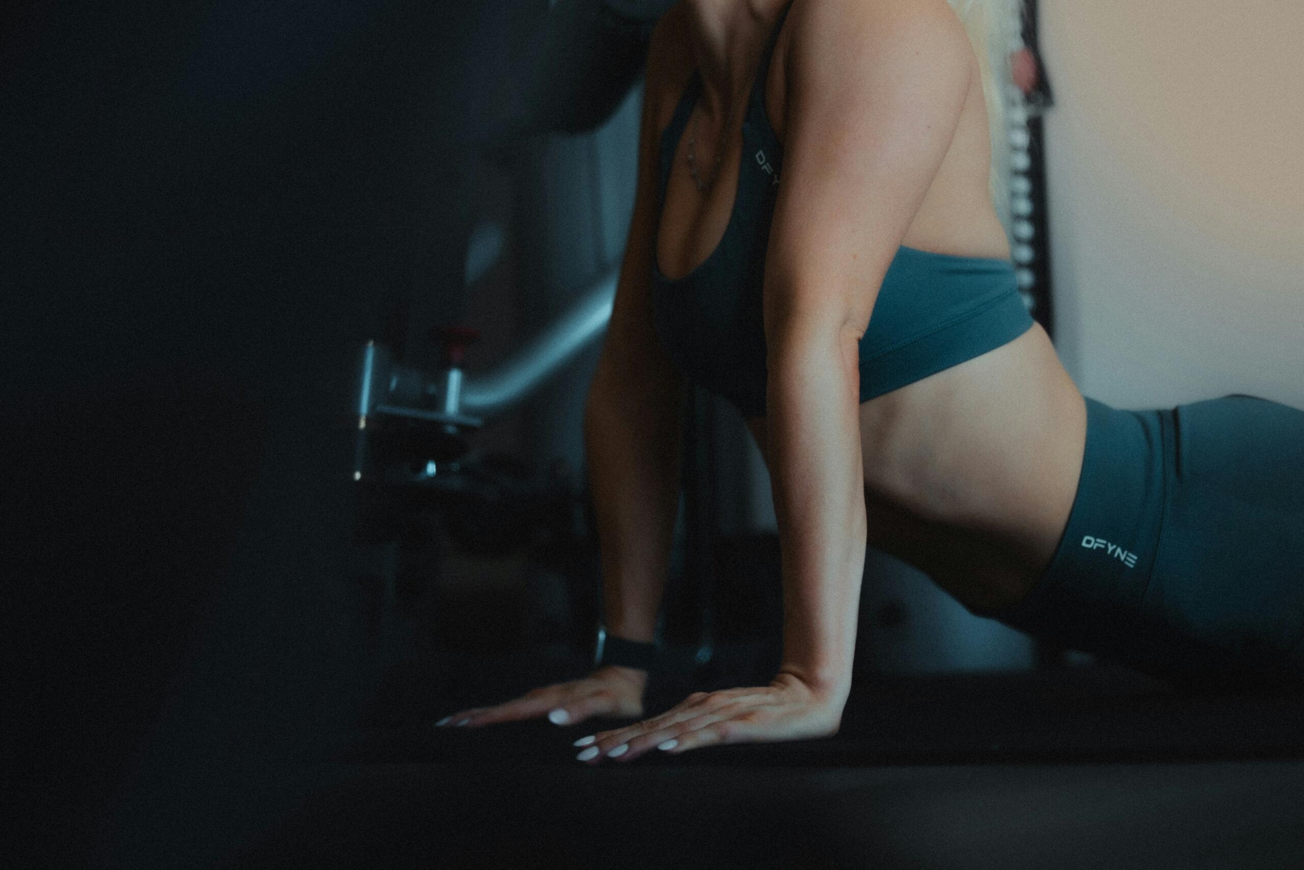 Mujer haciendo ejercicio de estiramiento tipo cobra en un gimnasio con luz tenue.