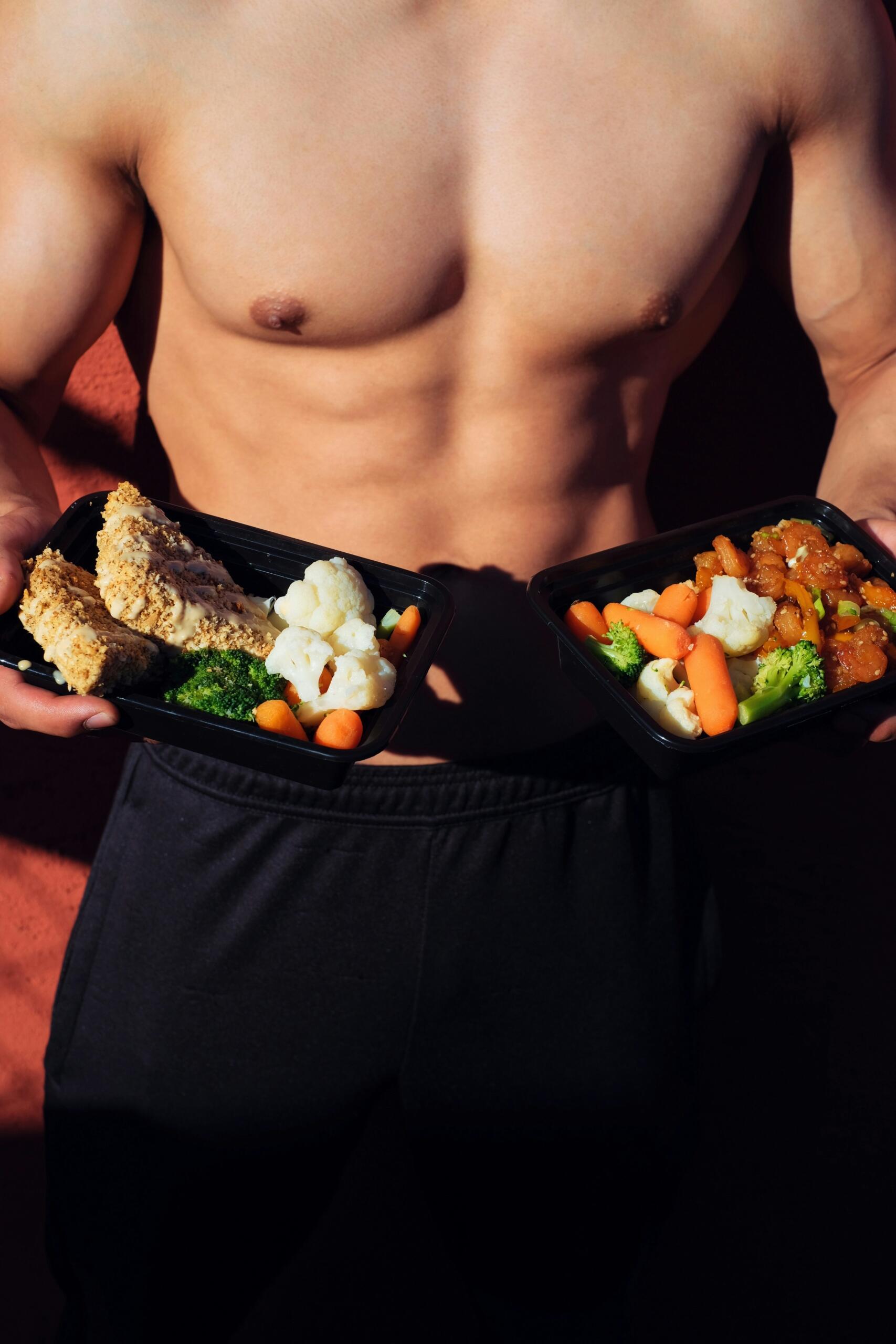 Cuerpo fitness masculino mostrando comidas saludables en recipientes con vegetales y proteínas.