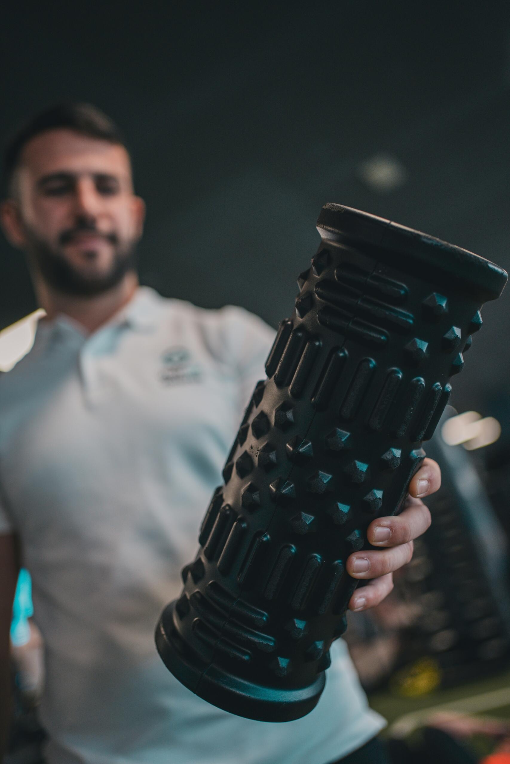 Entrenador sosteniendo un rodillo de masaje texturizado para terapia y recuperación deportiva.