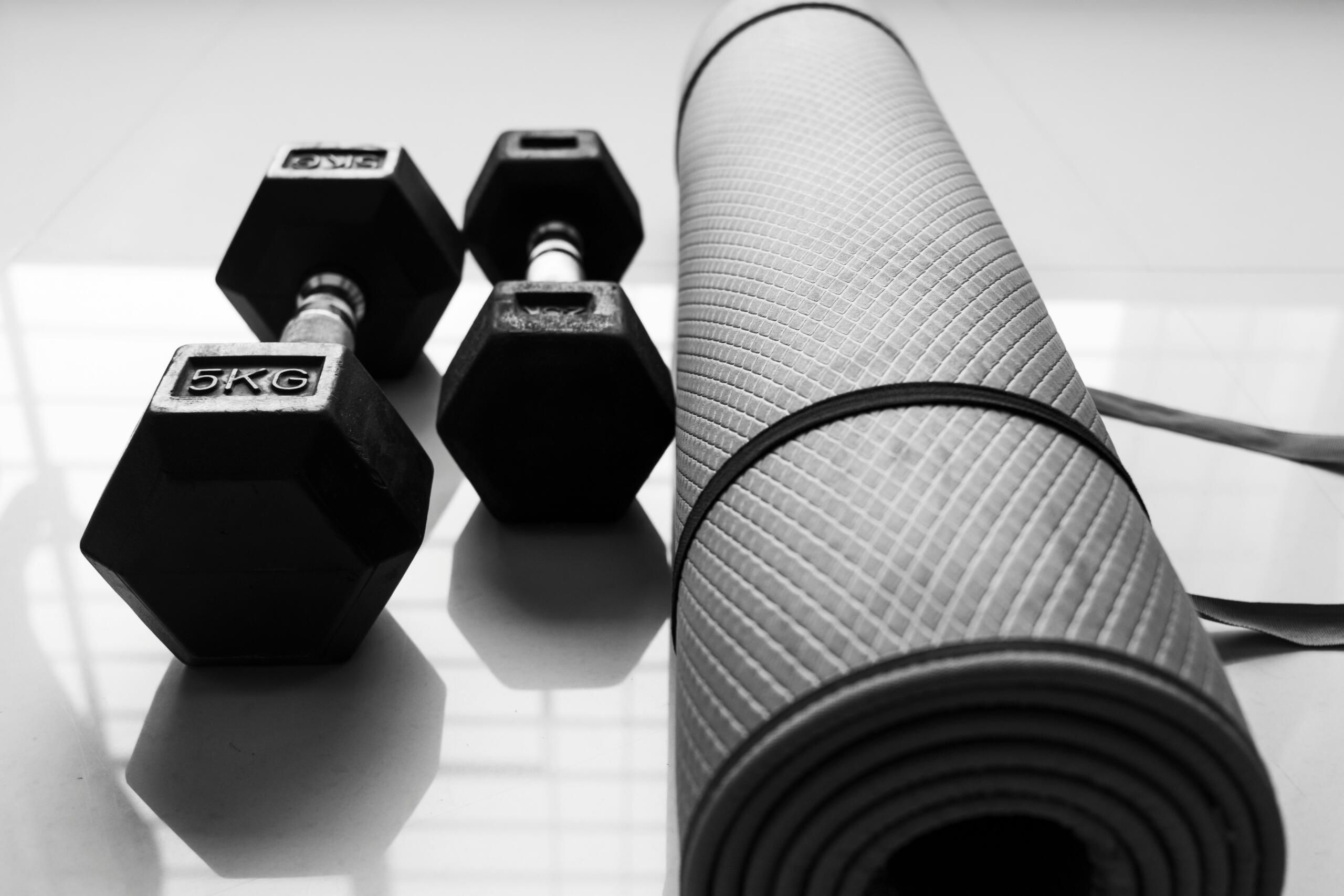 Mancuernas de 5 kg y esterilla de yoga en suelo brillante para entrenamiento funcional.