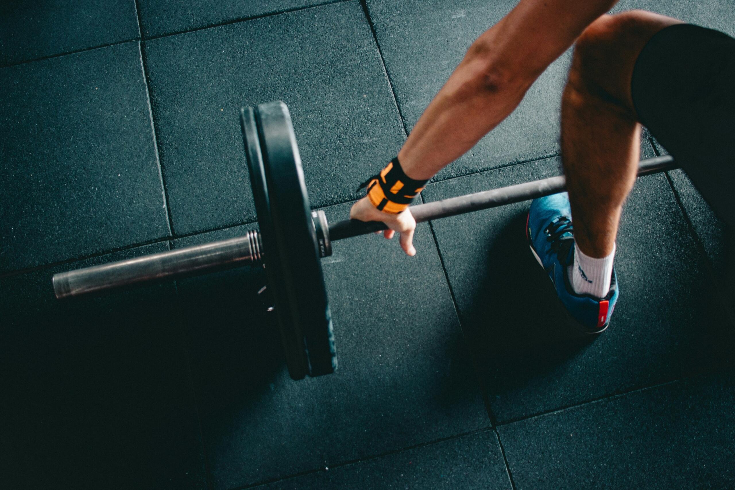 Deportista sujetando una barra con discos en el gimnasio, listo para levantar peso muerto.