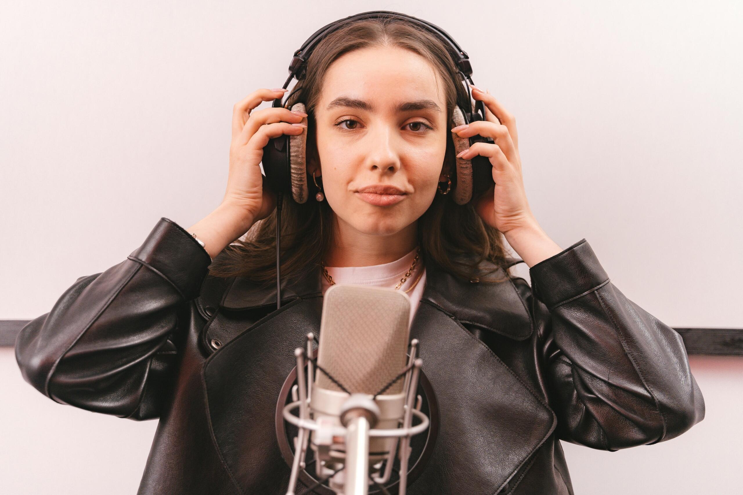 Cantante con auriculares y chaqueta de cuero frente a micrófono de condensador, grabación vocal en estudio moderno.