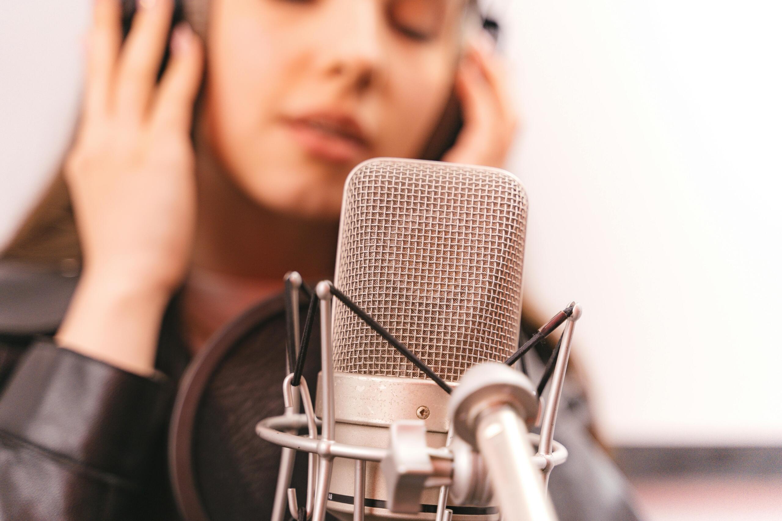 Cantante femenina grabando en estudio profesional con micrófono de condensador y auriculares, técnica vocal en acción.