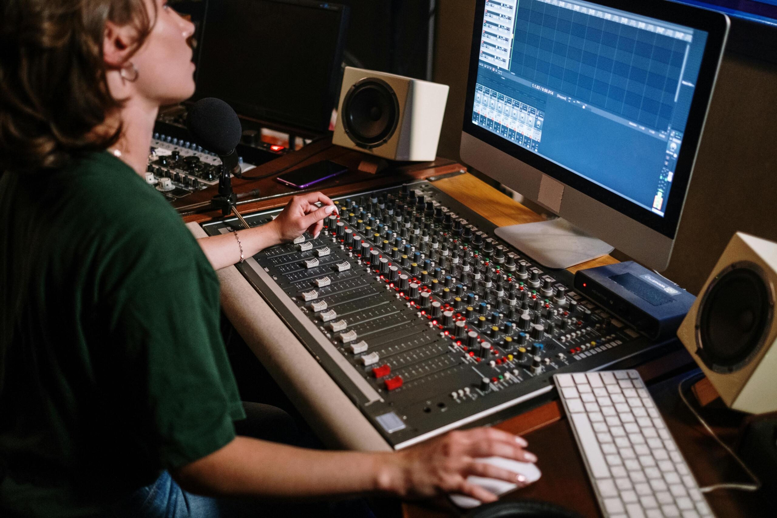 Productora ajustando niveles en consola de audio durante sesión de grabación, edición de pistas vocales en estudio moderno.