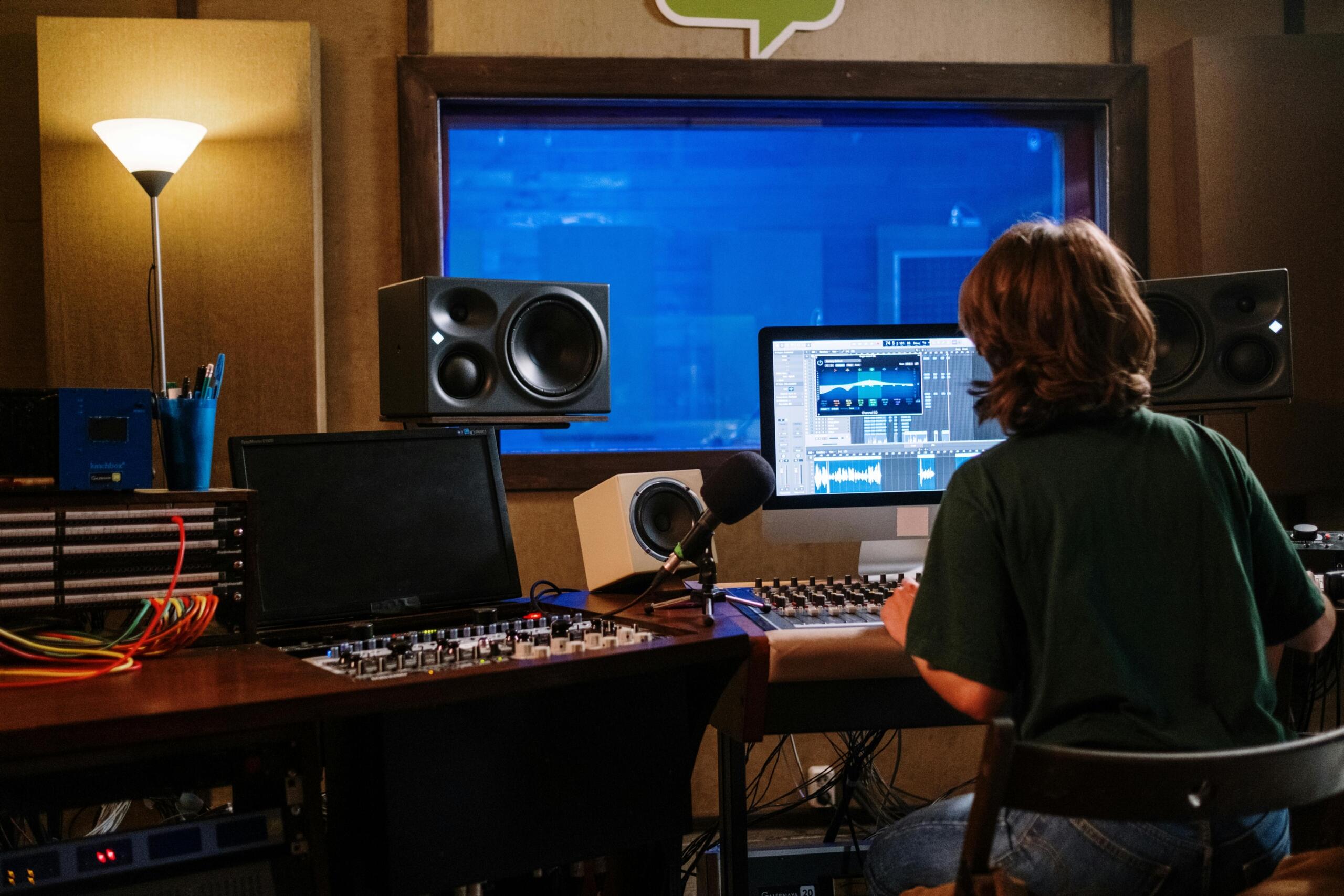 Productora trabajando en software de edición de audio en estudio de grabación, con monitores de estudio y consola de mezcla.