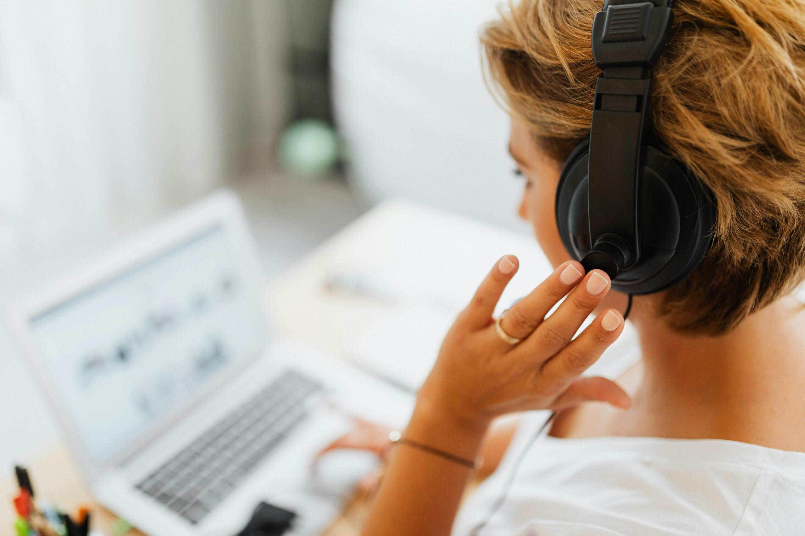 Mujer con auriculares grandes escuchando audio en laptop, entrenamiento de oído musical.