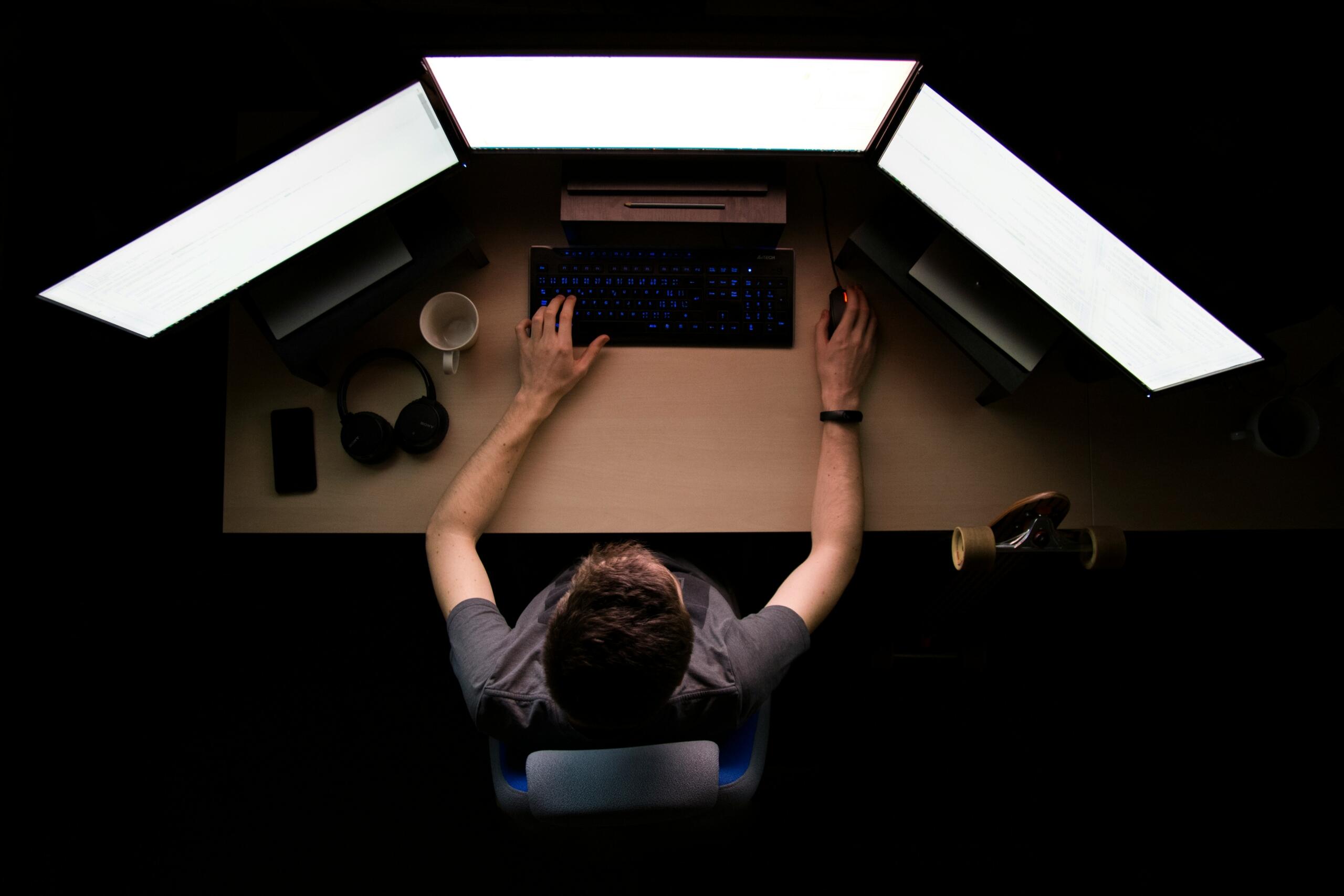 Programador trabajando de noche con tres monitores.