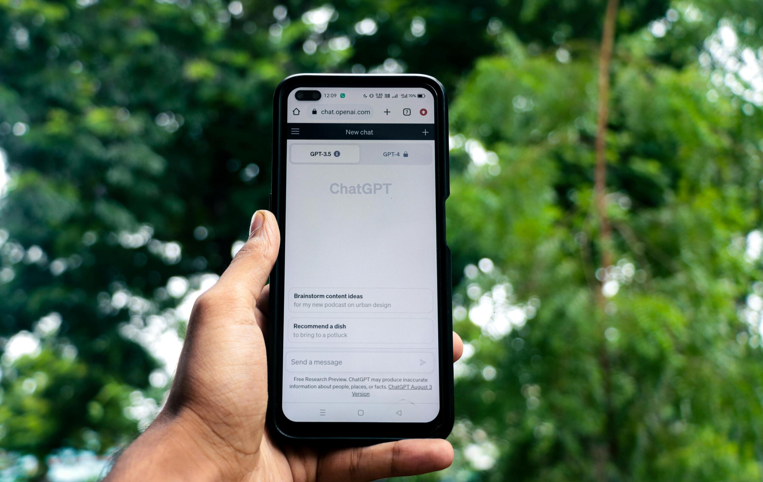 Pantalla de teléfono móvil con ChatGPT abierto en el navegador, sostenido por una mano al aire libre.
