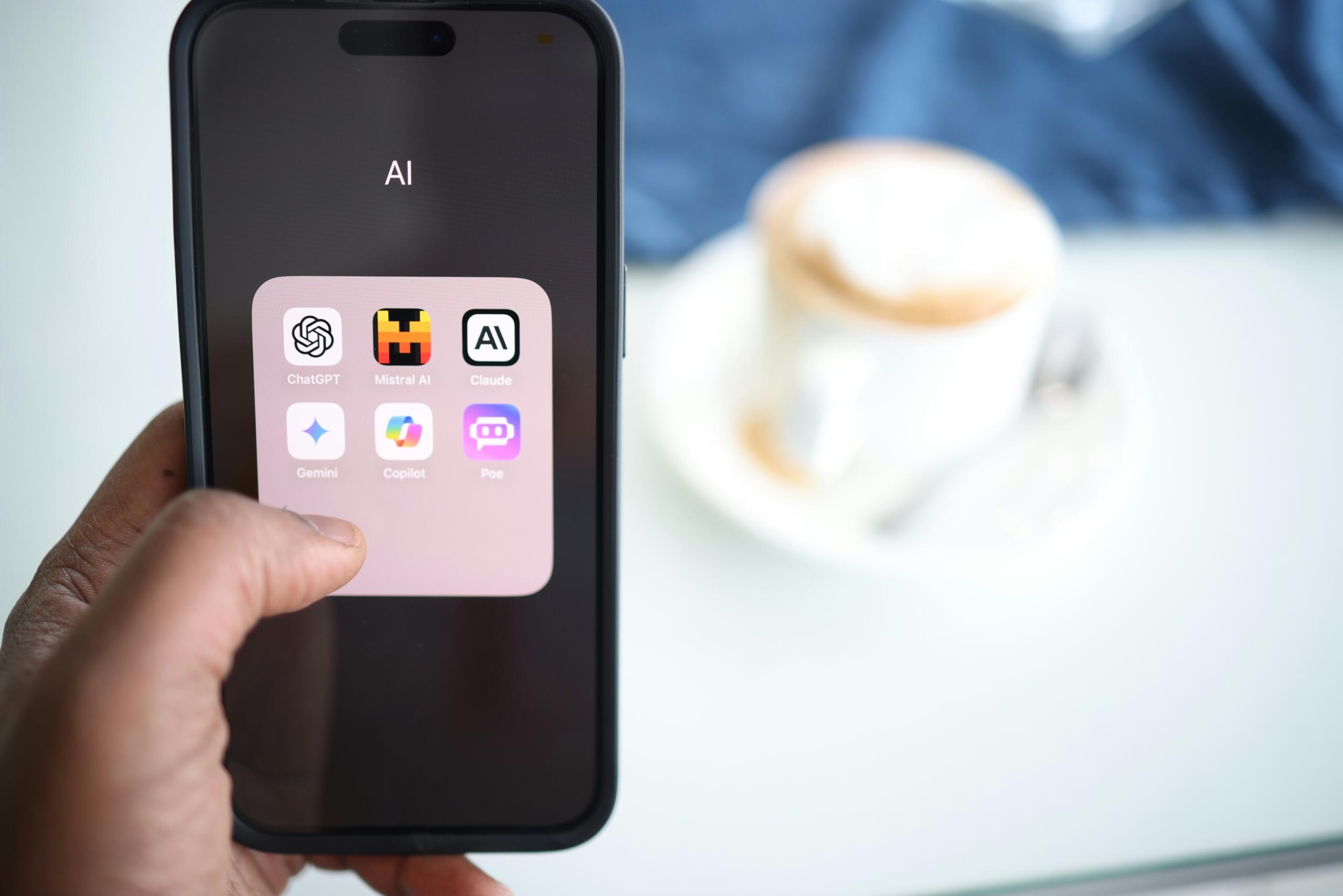 Pantalla de smartphone con aplicaciones de inteligencia artificial y taza de café al fondo.