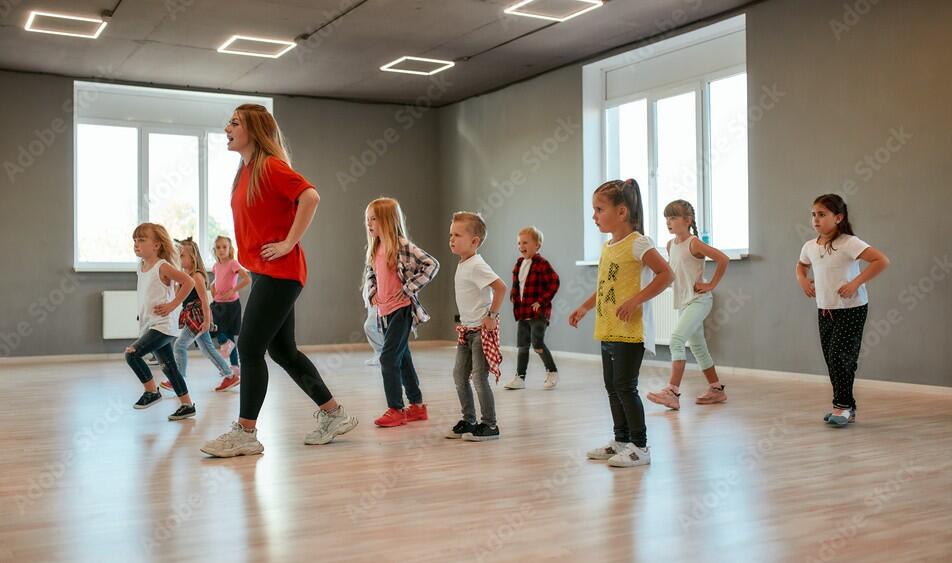 Learning how to move. Group of little boys and girls dancing while having choreography class in the dance studio. Female dance teacher and children