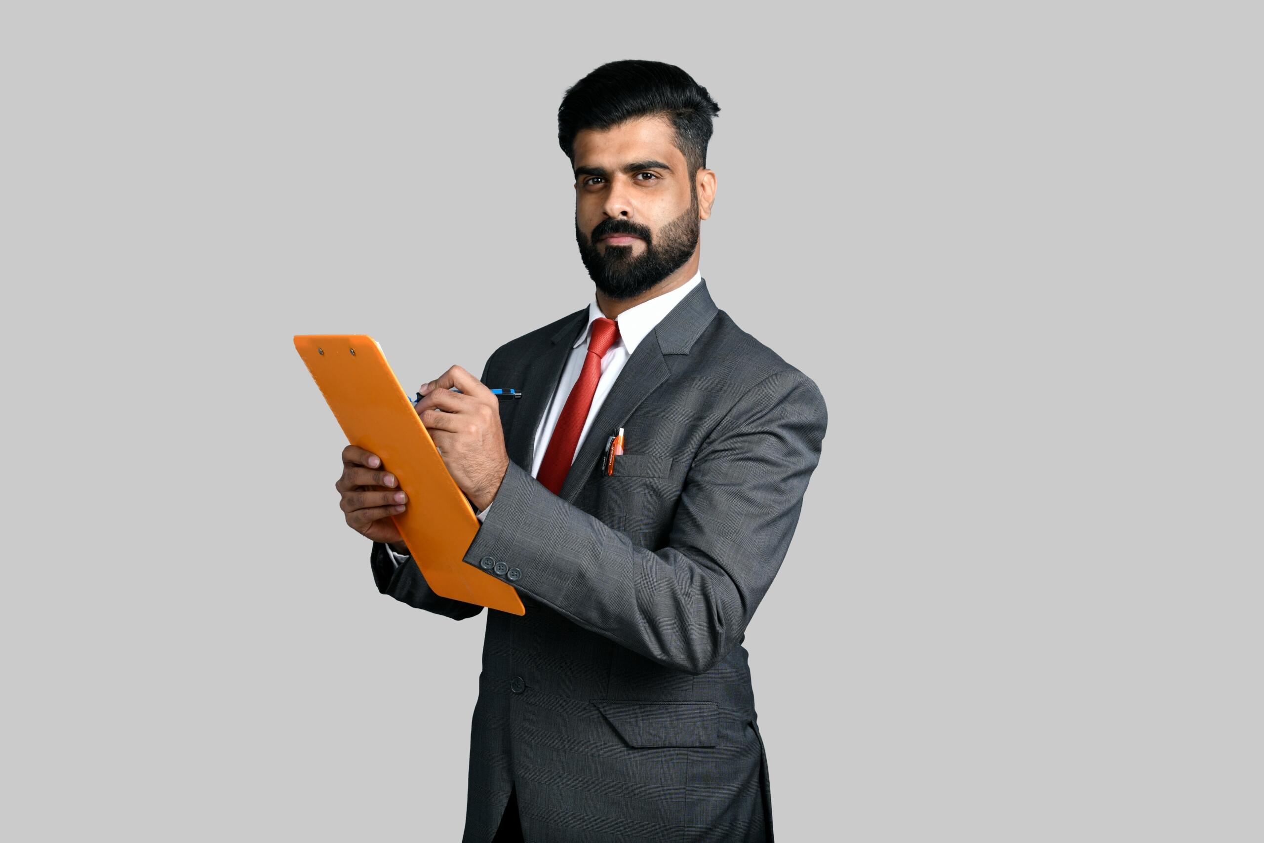 Hombre de negocios con traje y corbata roja sosteniendo un portapapeles naranja y escribiendo con un bolígrafo.