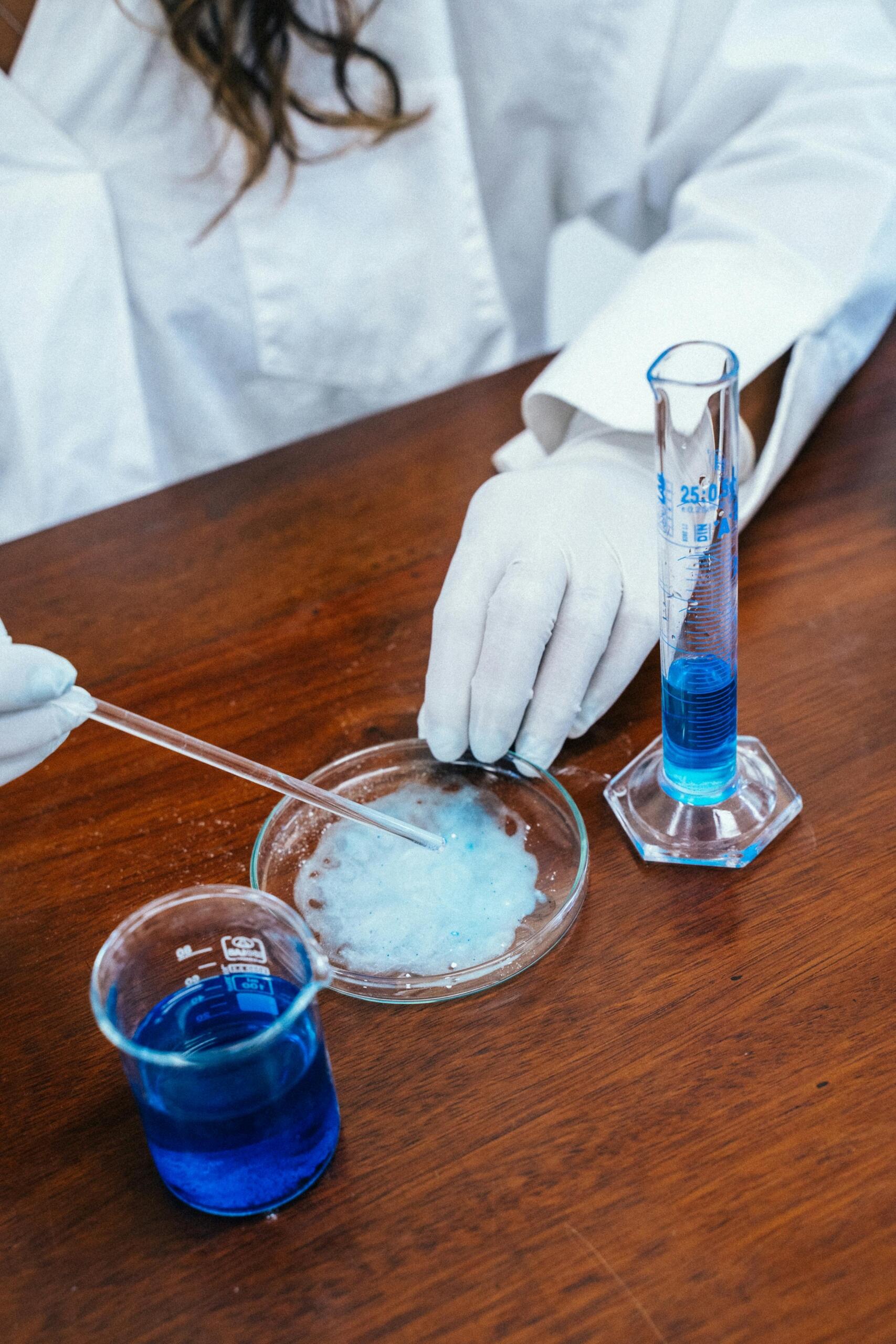 Estudiante realiza pipeteo sobre placa de Petri con reactivo azul; método científico, cultivos y técnicas básicas de laboratorio.