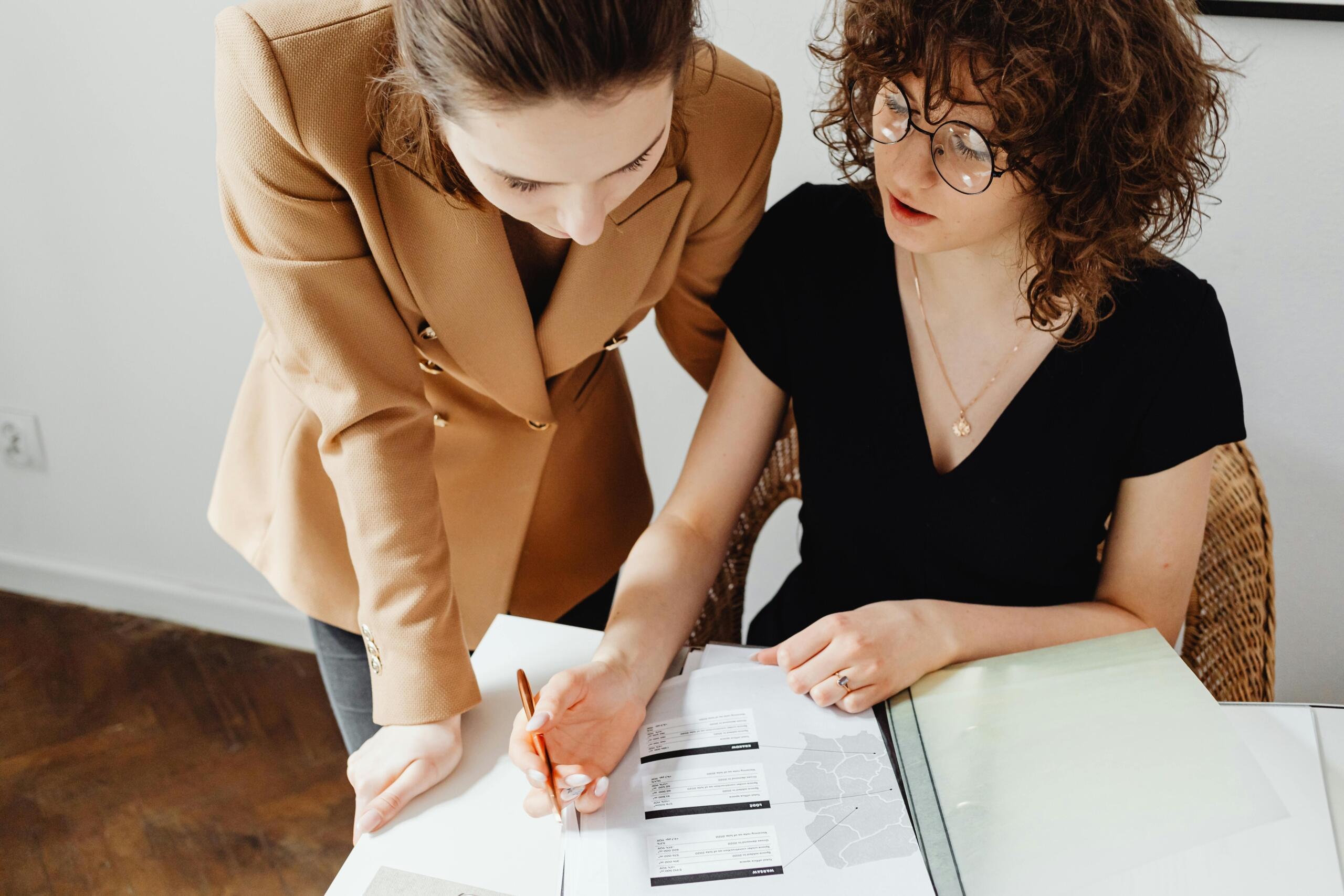 Dos mujeres revisando juntas un documento con gráficos y tablas, en un entorno de oficina, mientras analizan información contable.