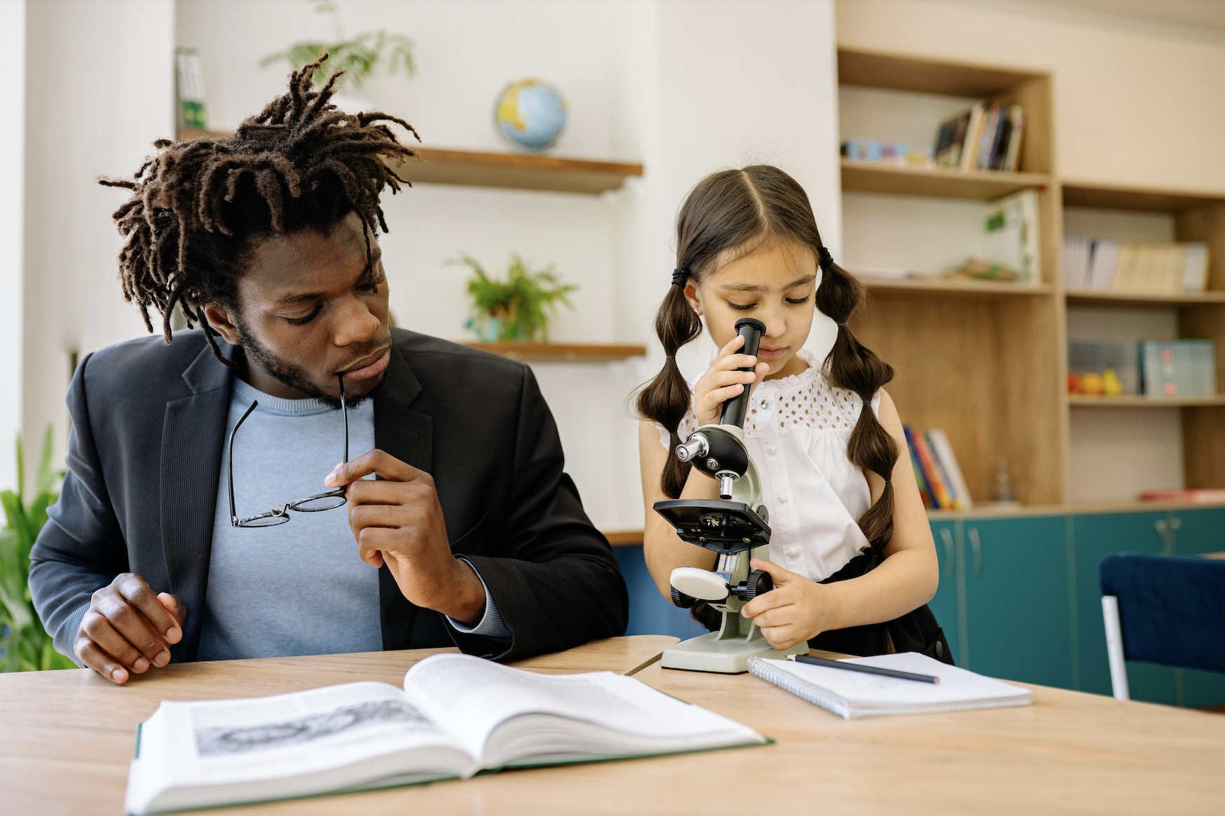 Niña descubre el mundo microscópico con apoyo de su mentor; educación STEM temprana y pasión por la biología en un ambiente educativo.