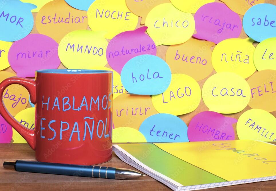 Study Spanish concept, a mug with written words Speak Spanish, notebook, pen and notes with common spanish words.