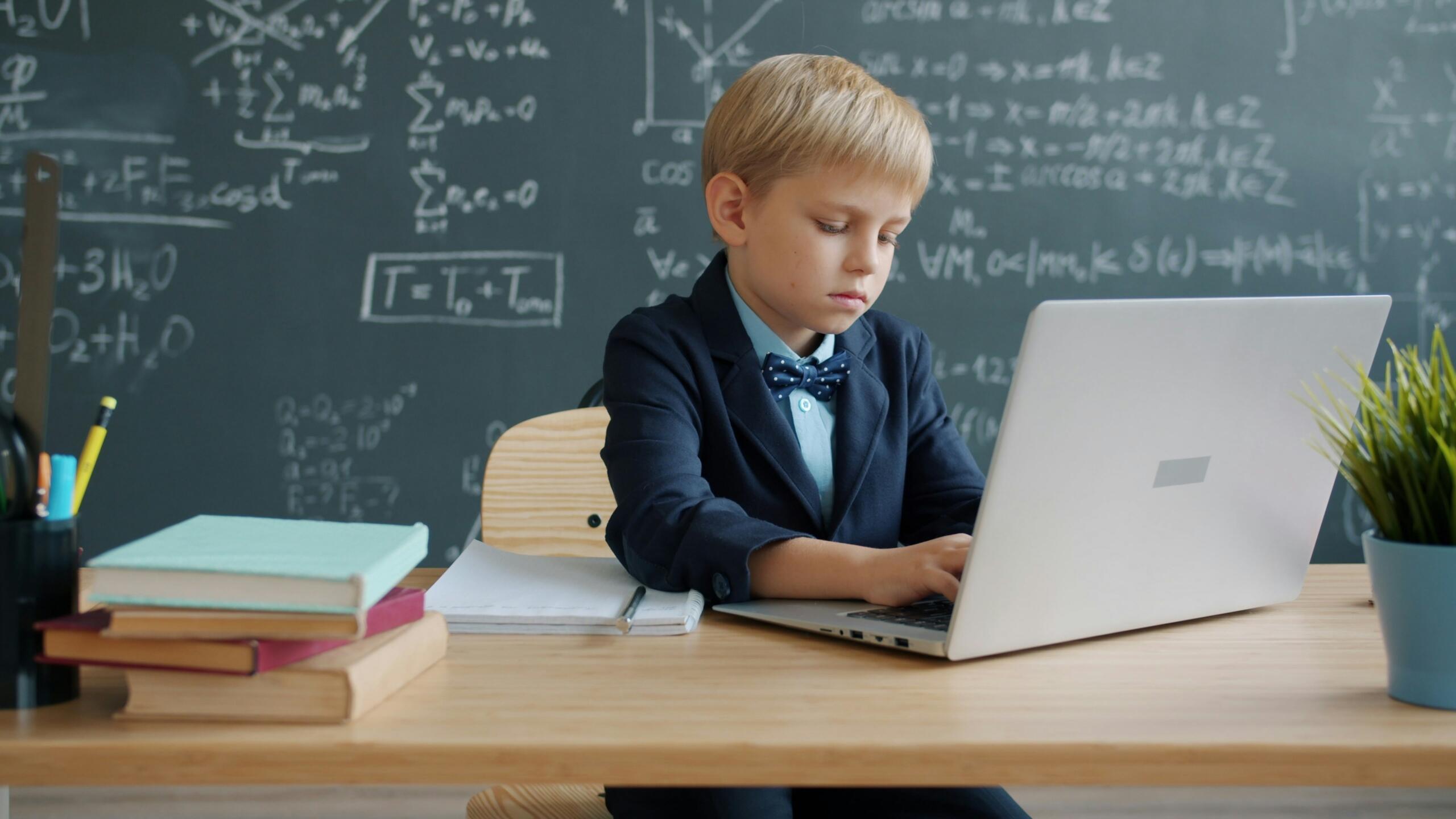Niño estudiando en línea con laptop frente a una pizarra llena de fórmulas matemáticas, ejemplo de educación moderna en Panamá.