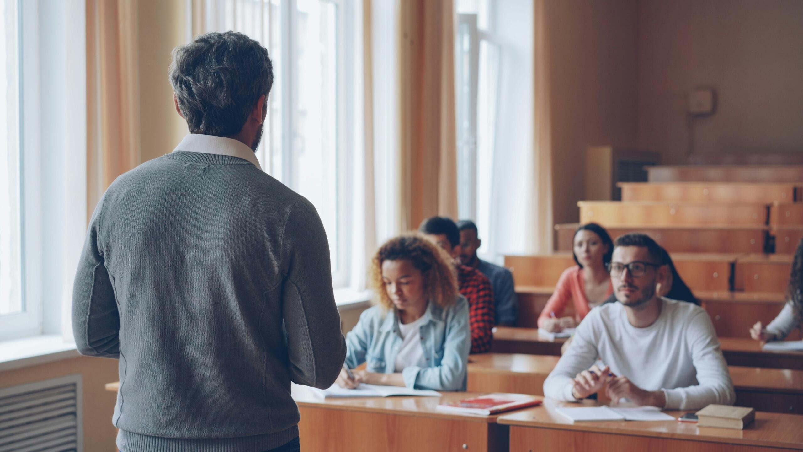 Profesor impartiendo clases presenciales a estudiantes universitarios en un aula iluminada en Panamá.