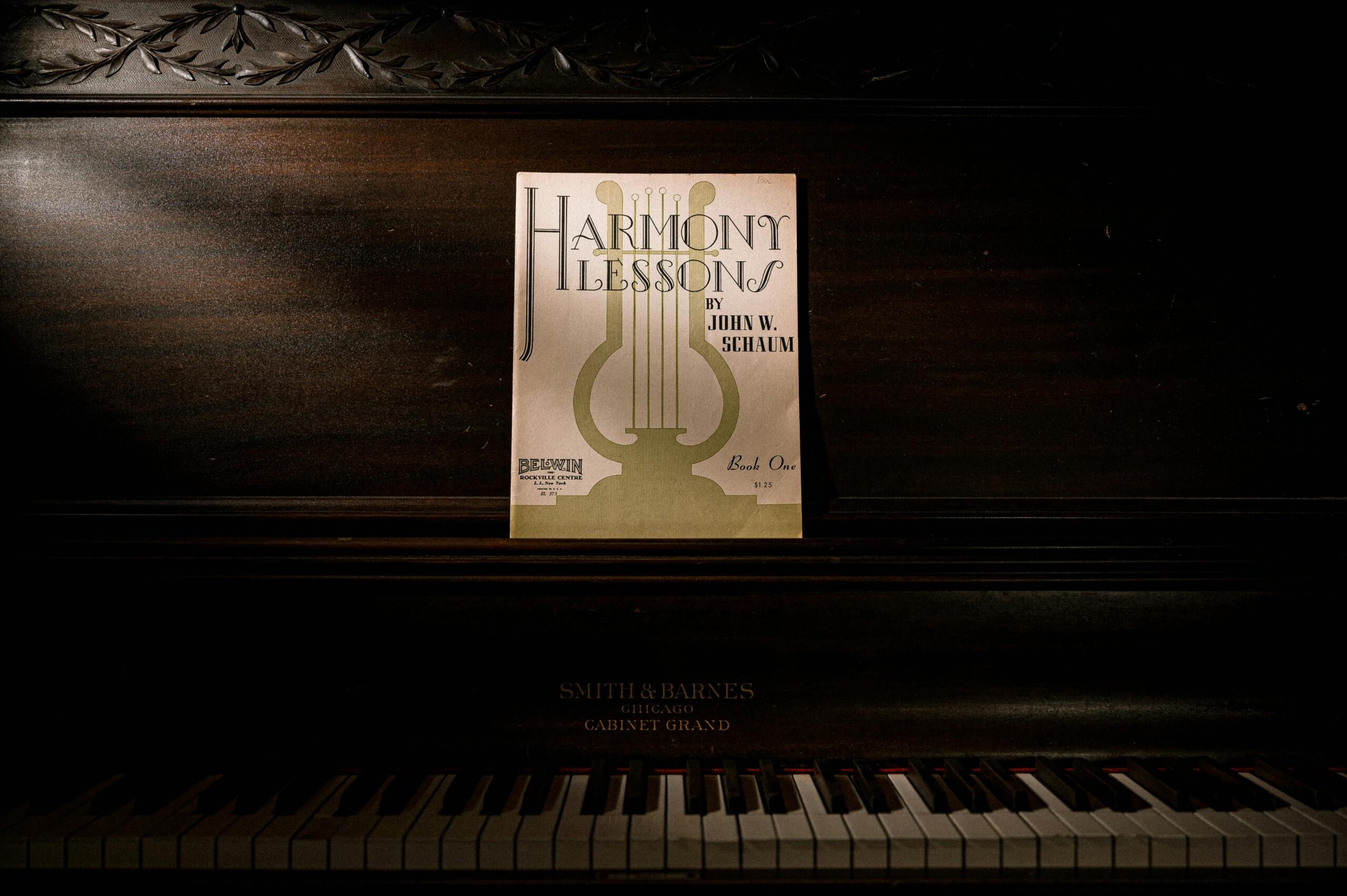 Libro de teoría musical “Harmony Lessons” colocado sobre un piano clásico, representando el estudio de armonía y piano.