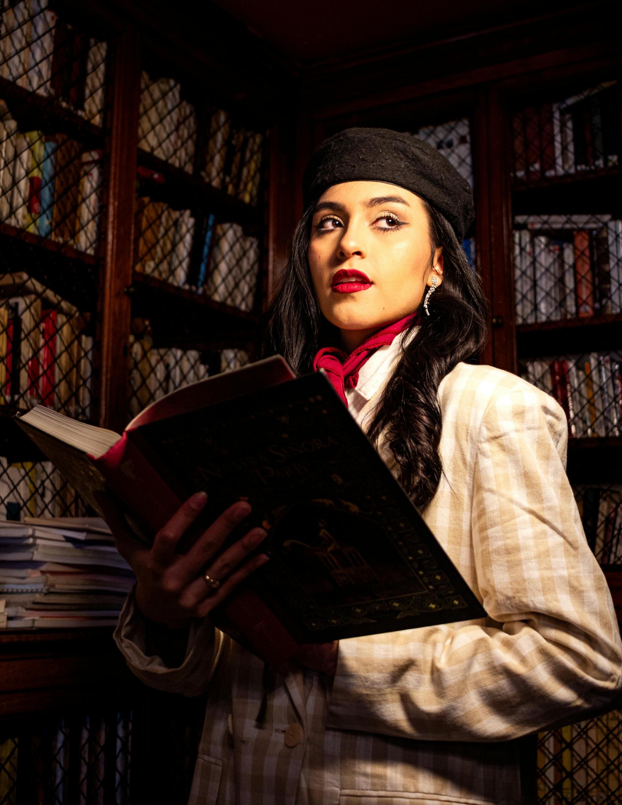 Mujer leyendo un libro en una biblioteca antigua, rodeada de estanterías con libros, en un ambiente de estudio y concentración.
