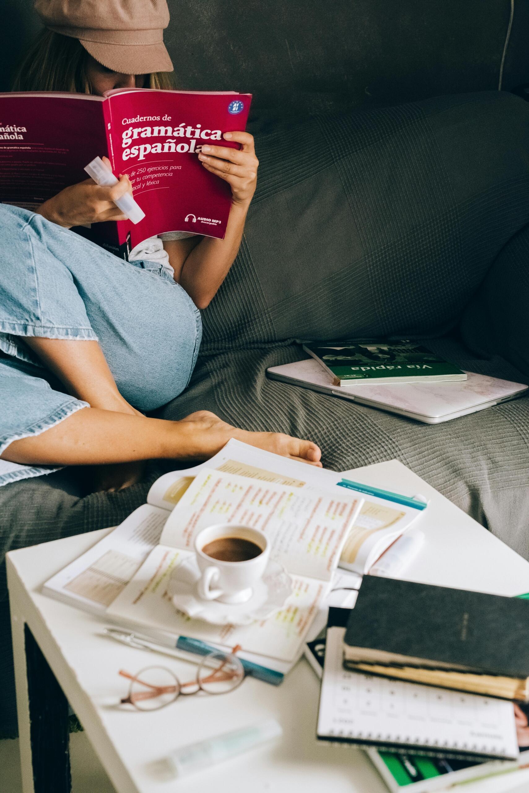 Estudiante leyendo un cuaderno de gramática española mientras estudia en el sofá.