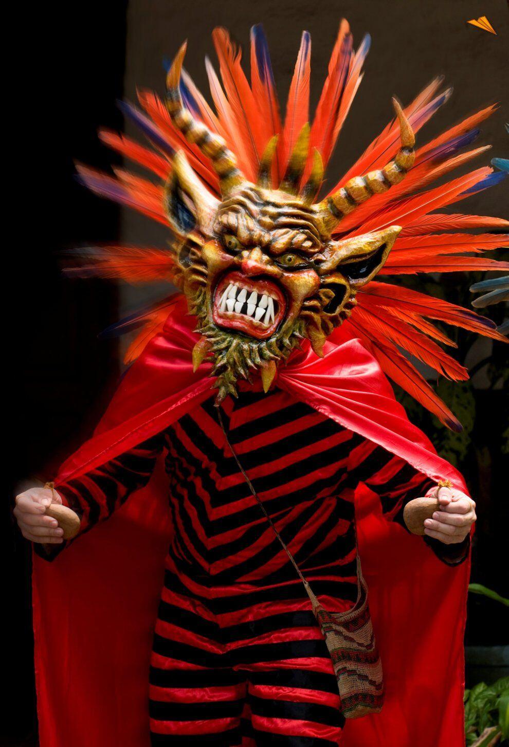 Diablico limpio con máscara dorada, cuernos y plumas rojas, traje rayado rojo y negro con capa.