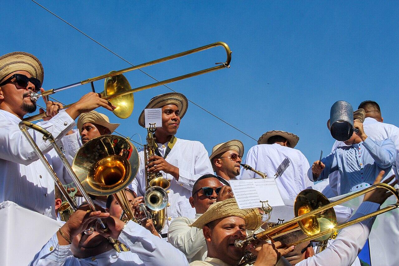 Murga panameña con músicos de blanco y sombreros pintados tocando trombones y saxofones.