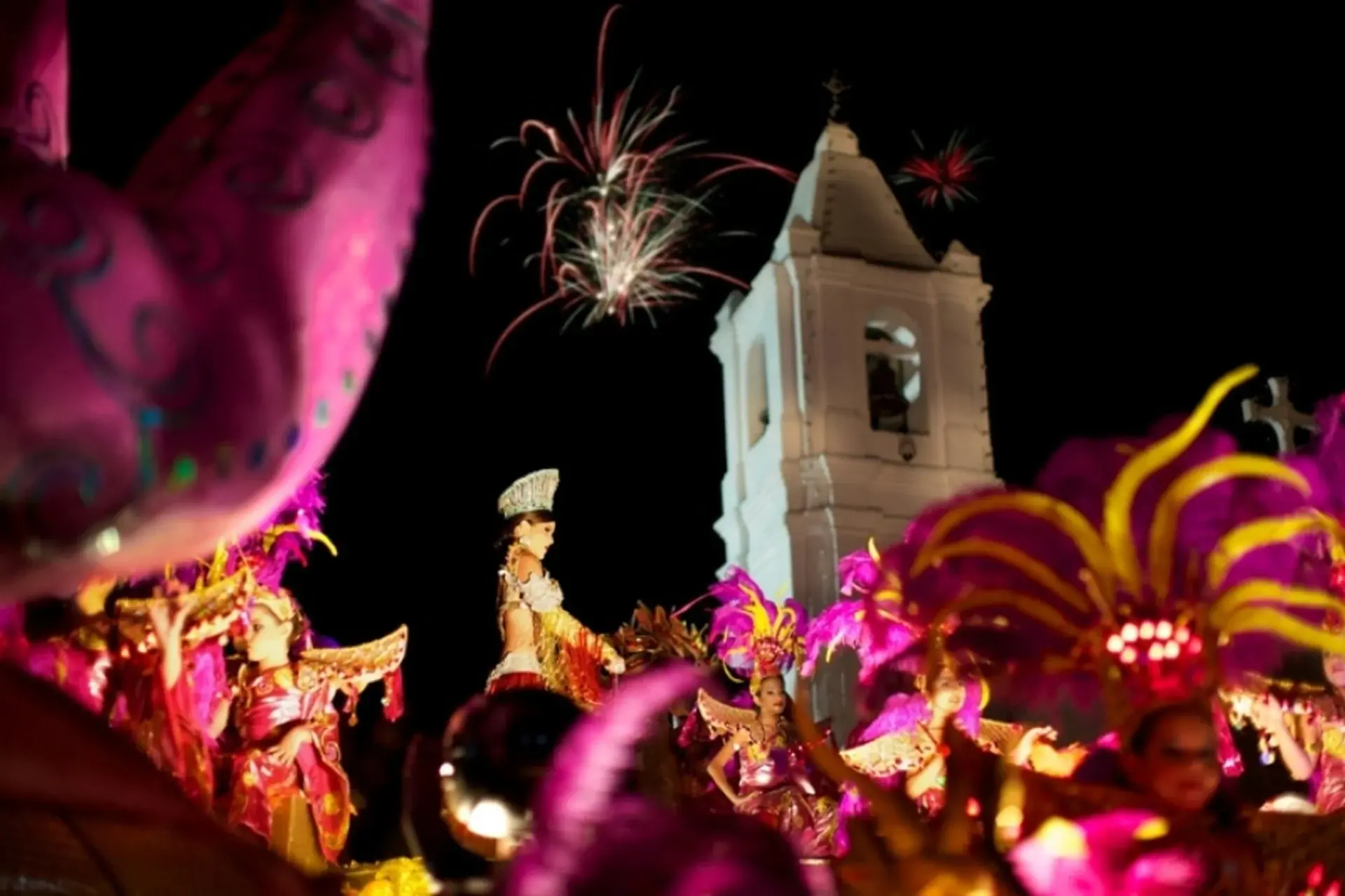 Desfile nocturno del Carnaval de Las Tablas con fuegos artificiales e iglesia colonial de fondo.