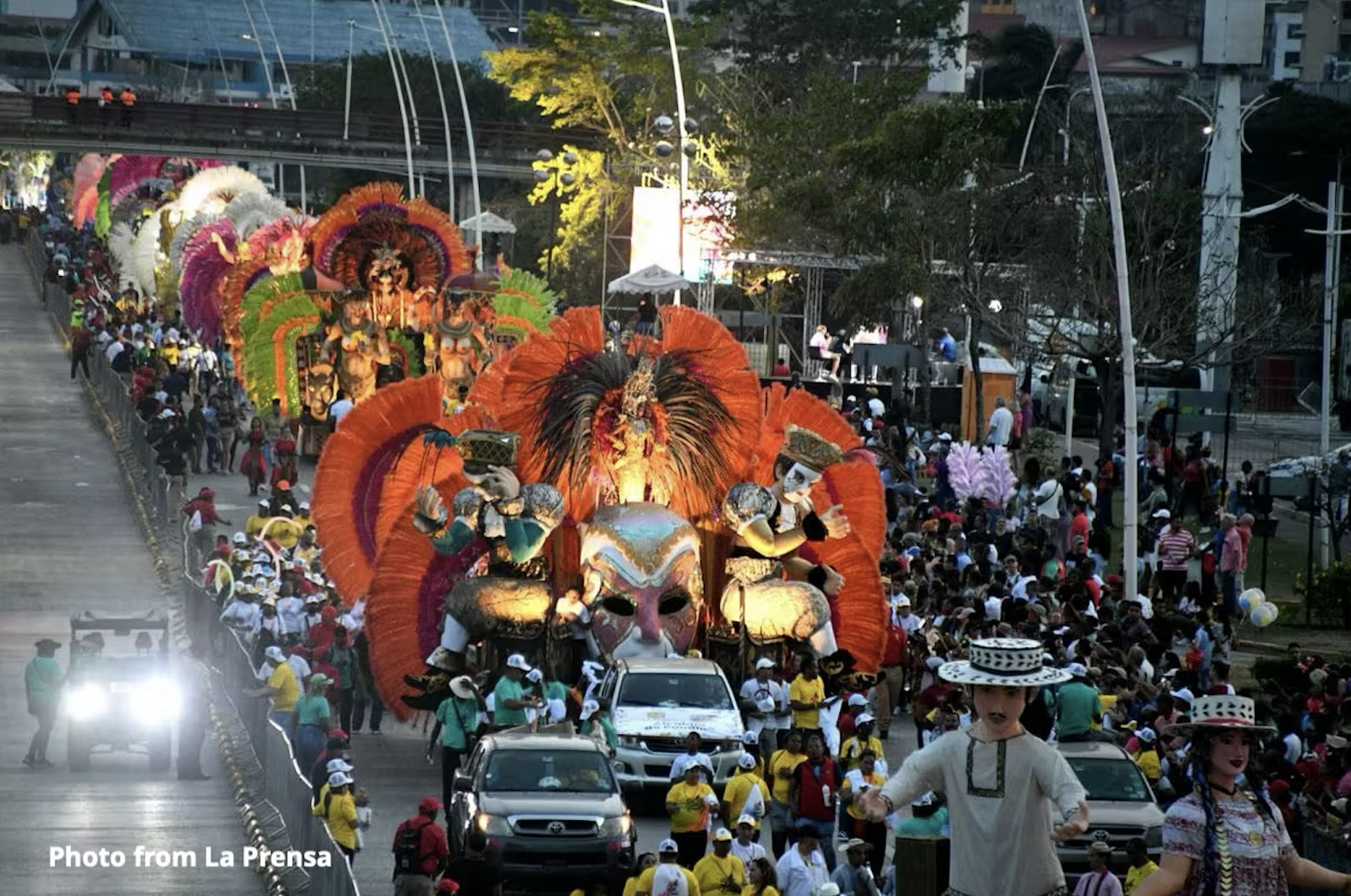 Desfile de carrozas coloridas con plumas naranjas y rojas en la Cinta Costera de Ciudad de Panamá.