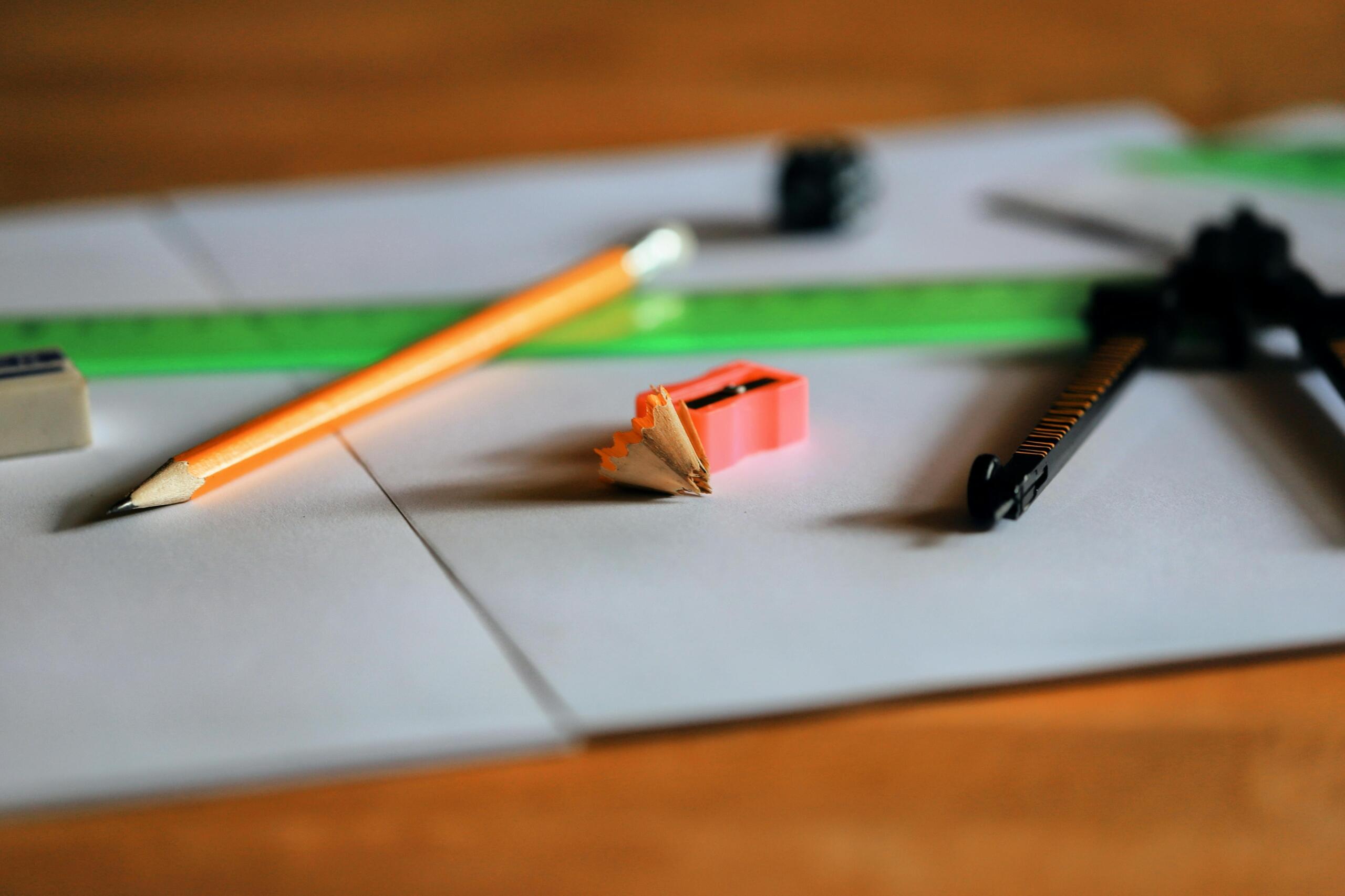 Útiles escolares para clase de geometría sobre escritorio de madera incluyendo lápiz, sacapuntas rosa, regla verde, compás y borrador con virutas de lápiz.