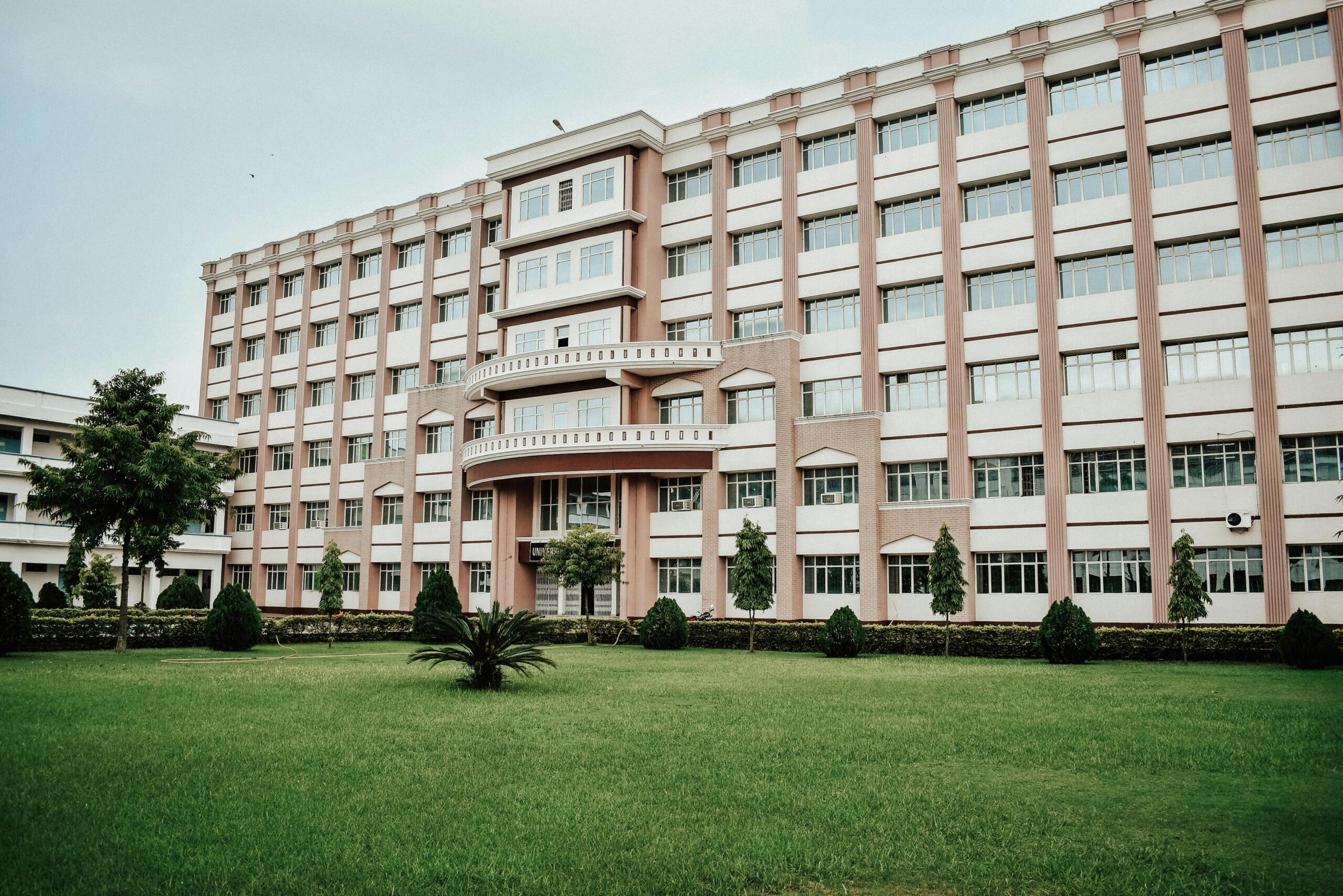 Fachada moderna de edificio universitario de varios pisos con jardines verdes, palmera y arbustos podados, ideal para representar instituciones de educación superior.
