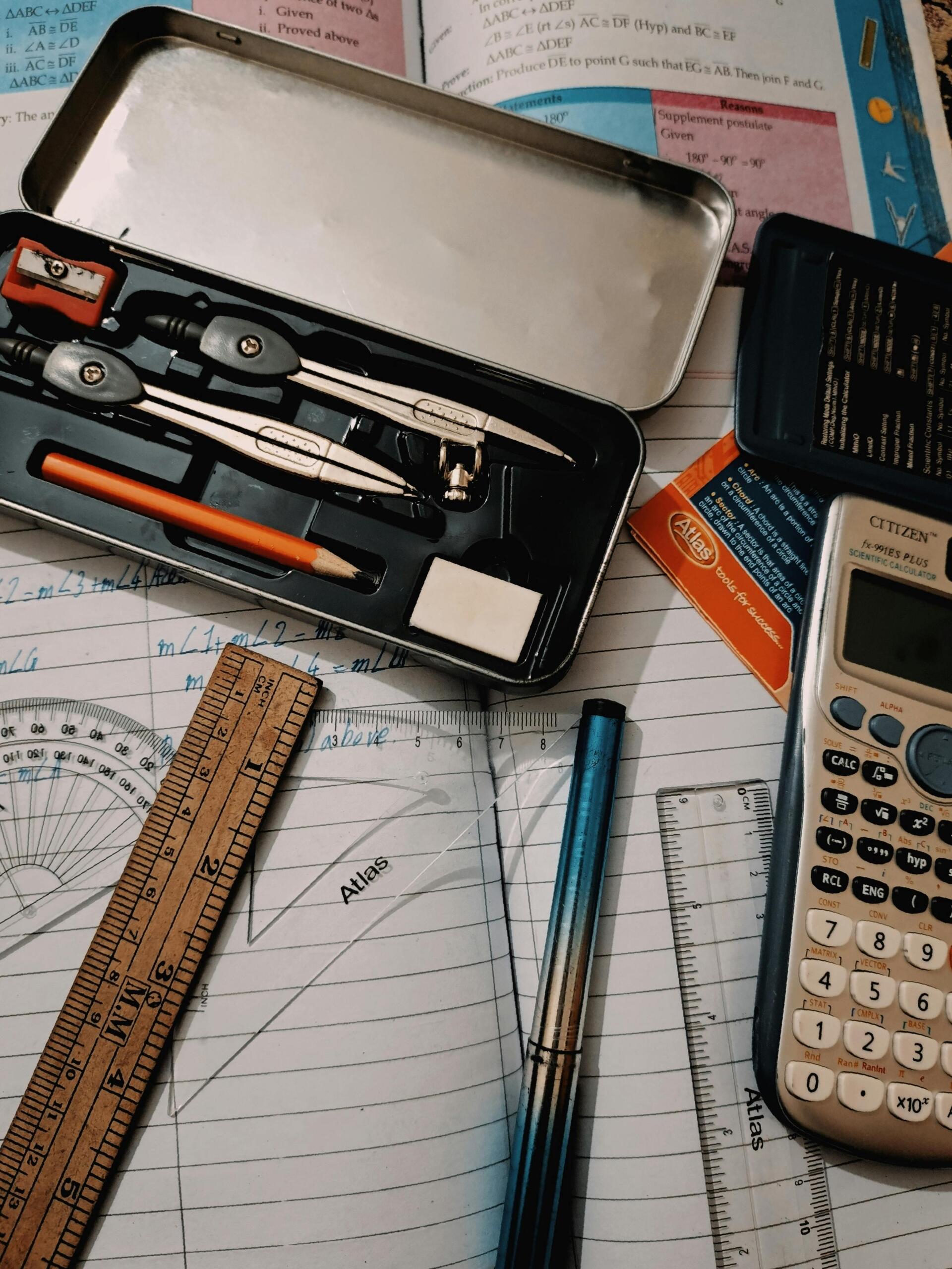 Vista cenital de kit completo de geometría con compás, calculadora científica Citizen, regla de madera, transportador y libro de texto sobre cuaderno con ejercicios resueltos.